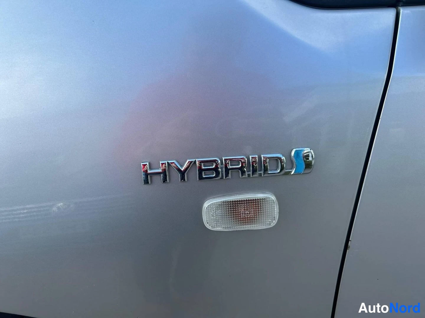 Edestä: Hybrid-merkki autonsäleikön lisävalon yläpuolella harmaassa koripanelissa.