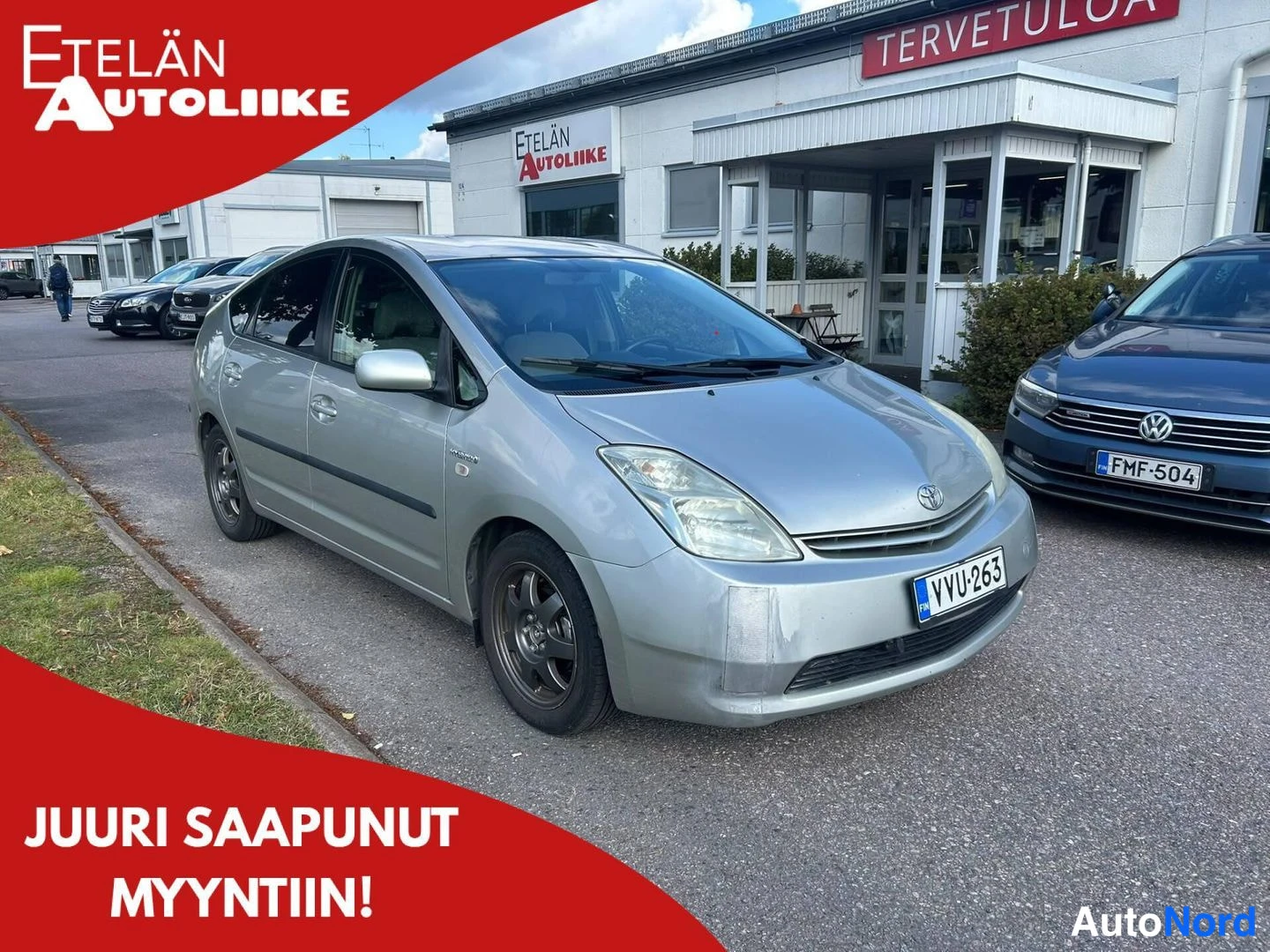 Etuviisto, nokka oikealle: Hopeanvärinen Toyota Prius etukulmasta autonhallin edustalla, rekisterikilpi.