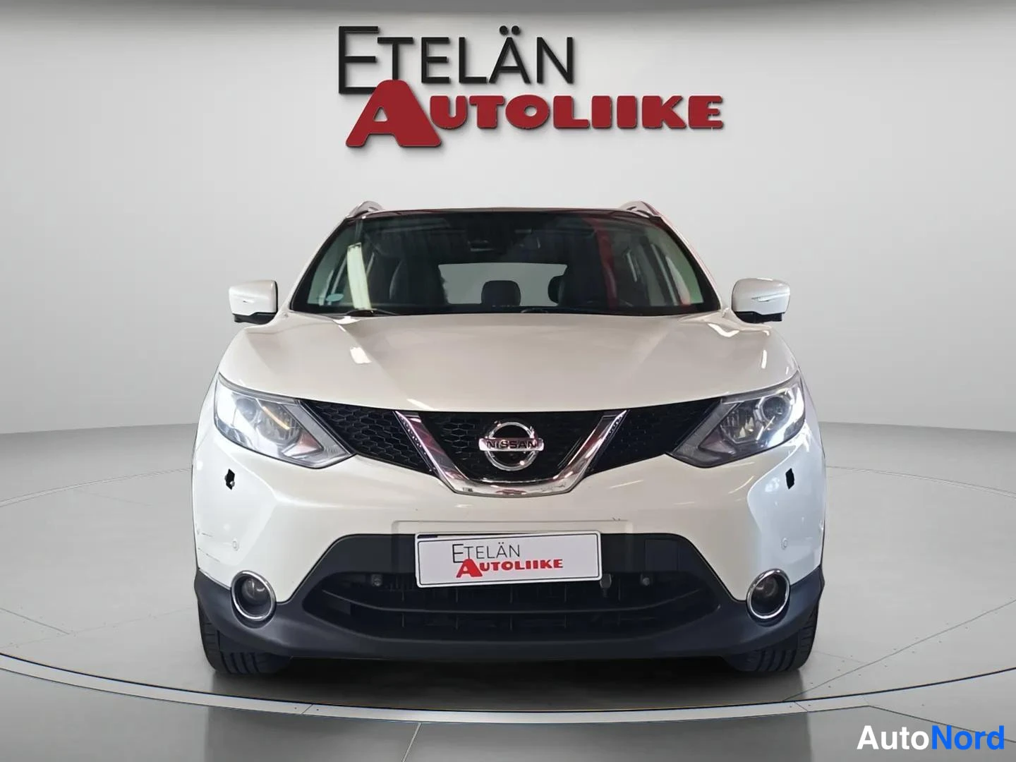 Edestä: Valkoisen Nissan Qashqain etunäkymä suoraan edestä studiovaalealla taustalla