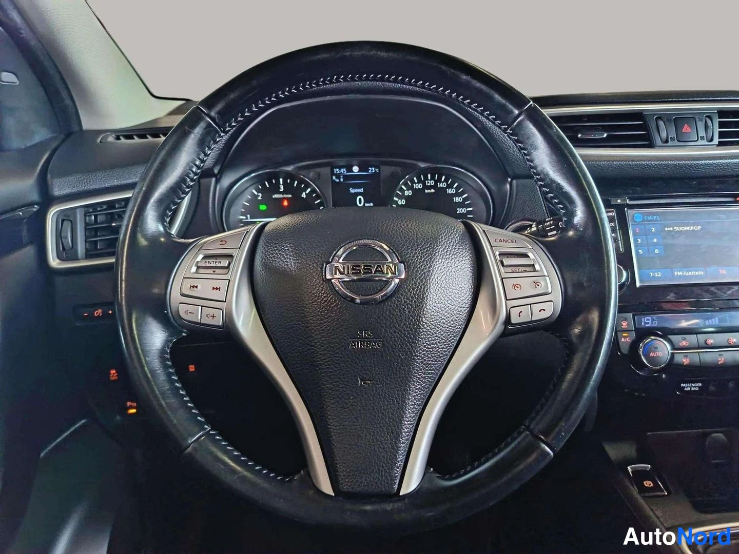 Etuviisto: Lähikuva Nissan-ohjauspyörästä, jonka napassa lukee SRS AIRBAG; kojetaulu ja osa keskikonsolin näytöstä näkyvät taustalla.