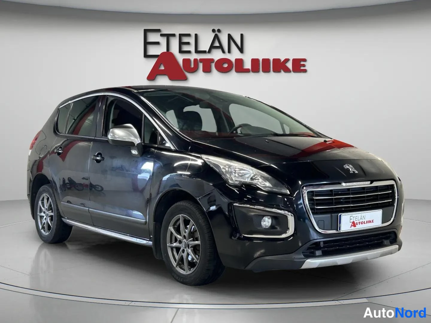 Etuviisto, nokka oikealle: Mustan farmarin(edustusauto) Peugeot etuviistossa oikealta, keulajalusta ja kyljet näkyvissä studiovalaistuksessa.