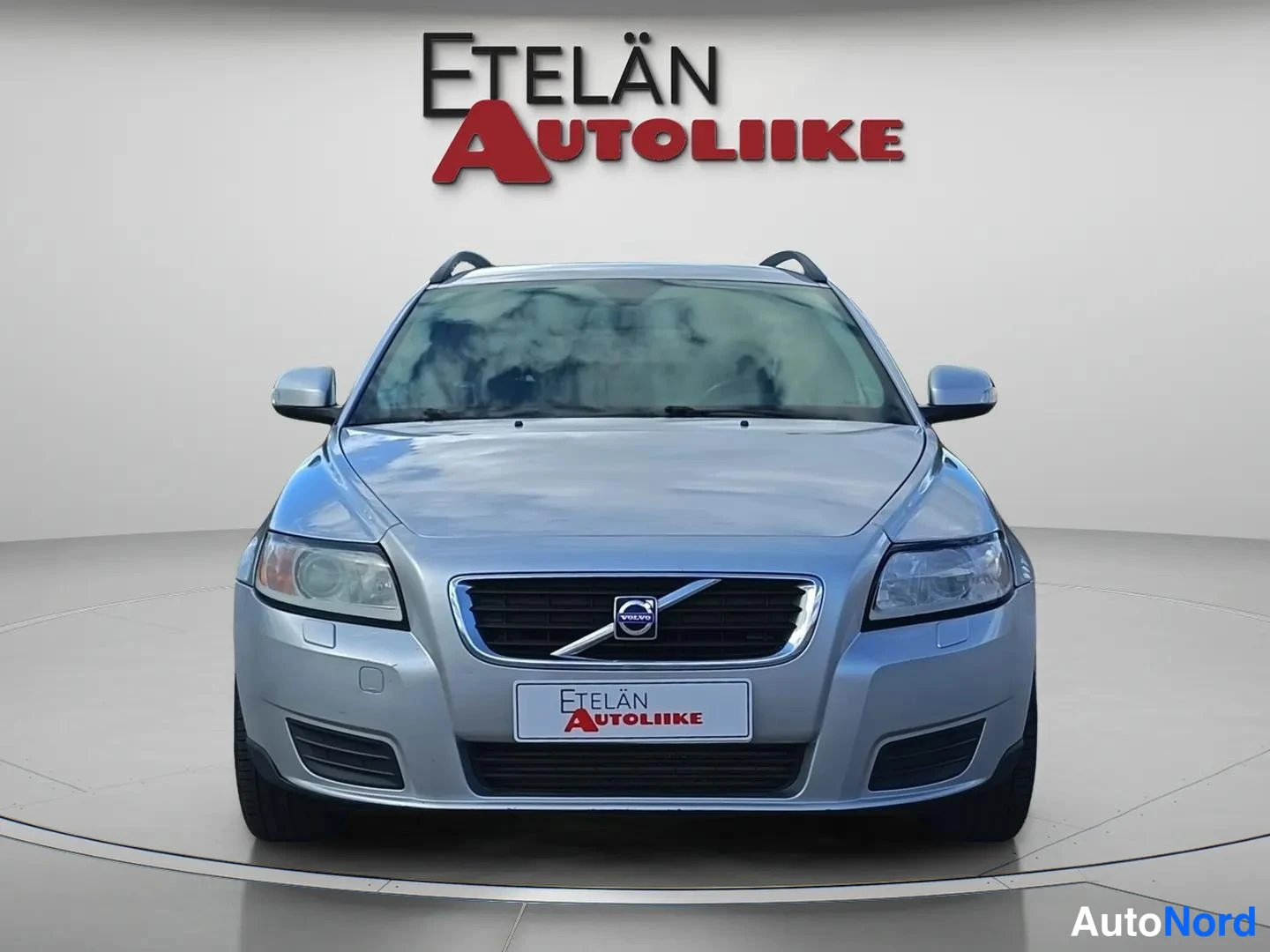 Edestä: Auto suoraan edestä kuvattuna, etusäleikön keskellä Volvo-tunnus, studiovaalea tausta.