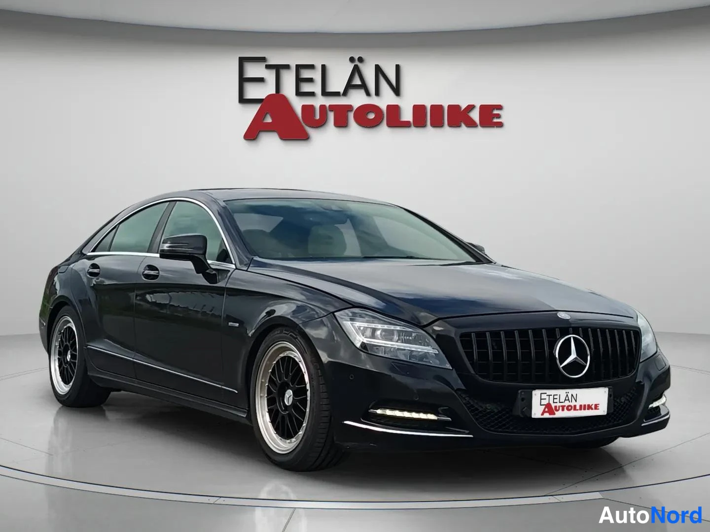 Etuviisto, nokka oikealle: Mustan Mercedes-Benzin etukolmallasivunäyttökuvan studiovalokuvassa, Etelän Autoliike -taustatunnus.