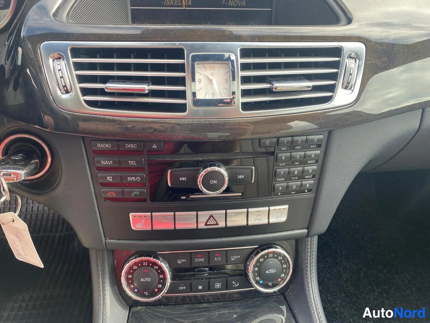Muu: Keskikonsolin lähikuva: ilmastointiautomaatti (AUTO), näppäimistö, radio/Navi/Tel-napit ja analoginen kello.