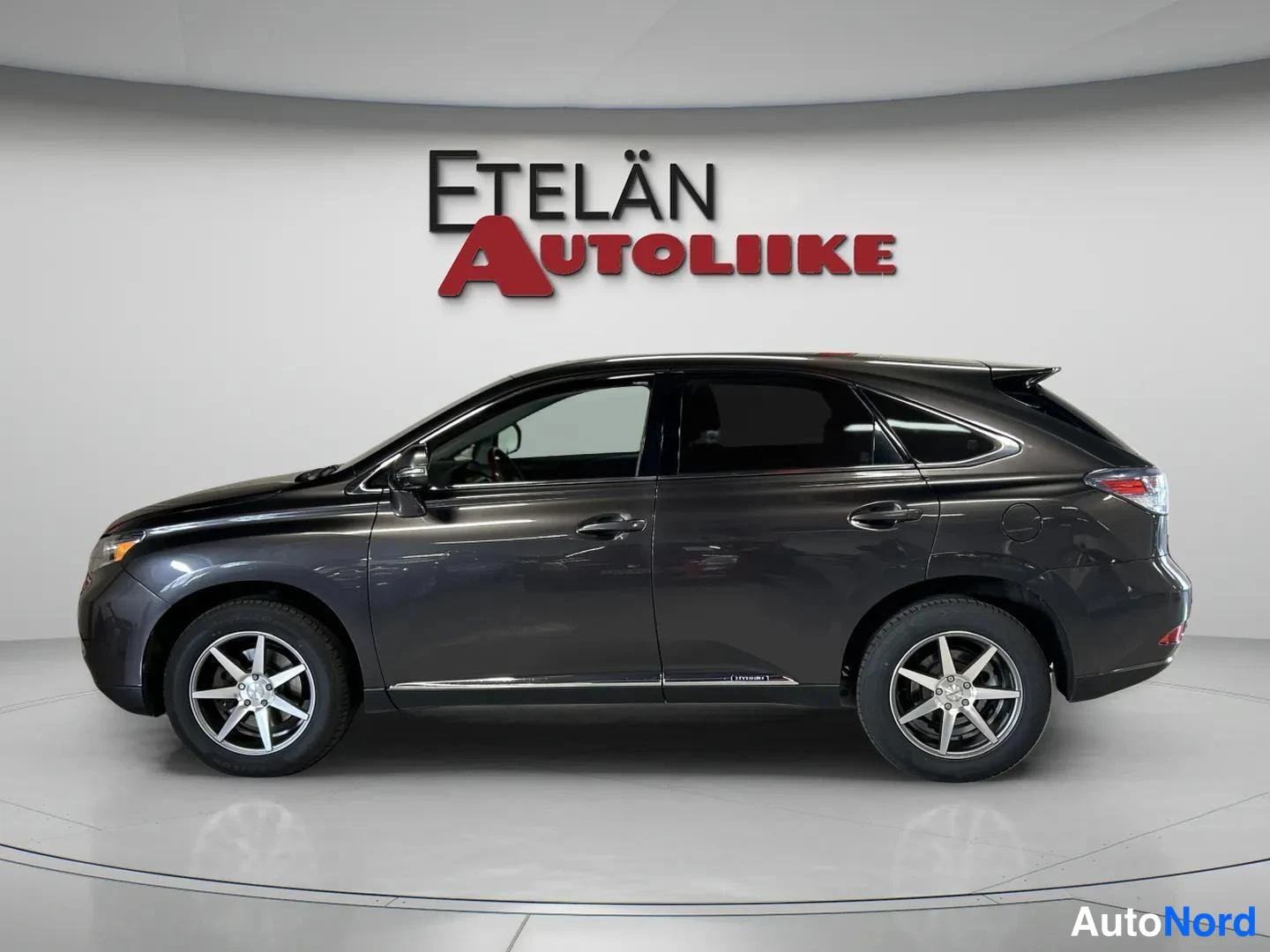 Takaviisto: Tummanharmaan Lexus RX -maasturin sivunäkymä, takavalo ja takapää näkyvät oikealla studiotaustaa vasten.