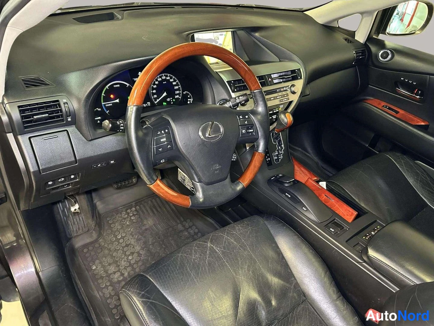 Muu: Kuljettajan näkymä: puureunuksinen Lexus-ohjauspyörä, hybridimittaristo ja keskikonsoli mustalla nahkasisustuksella.