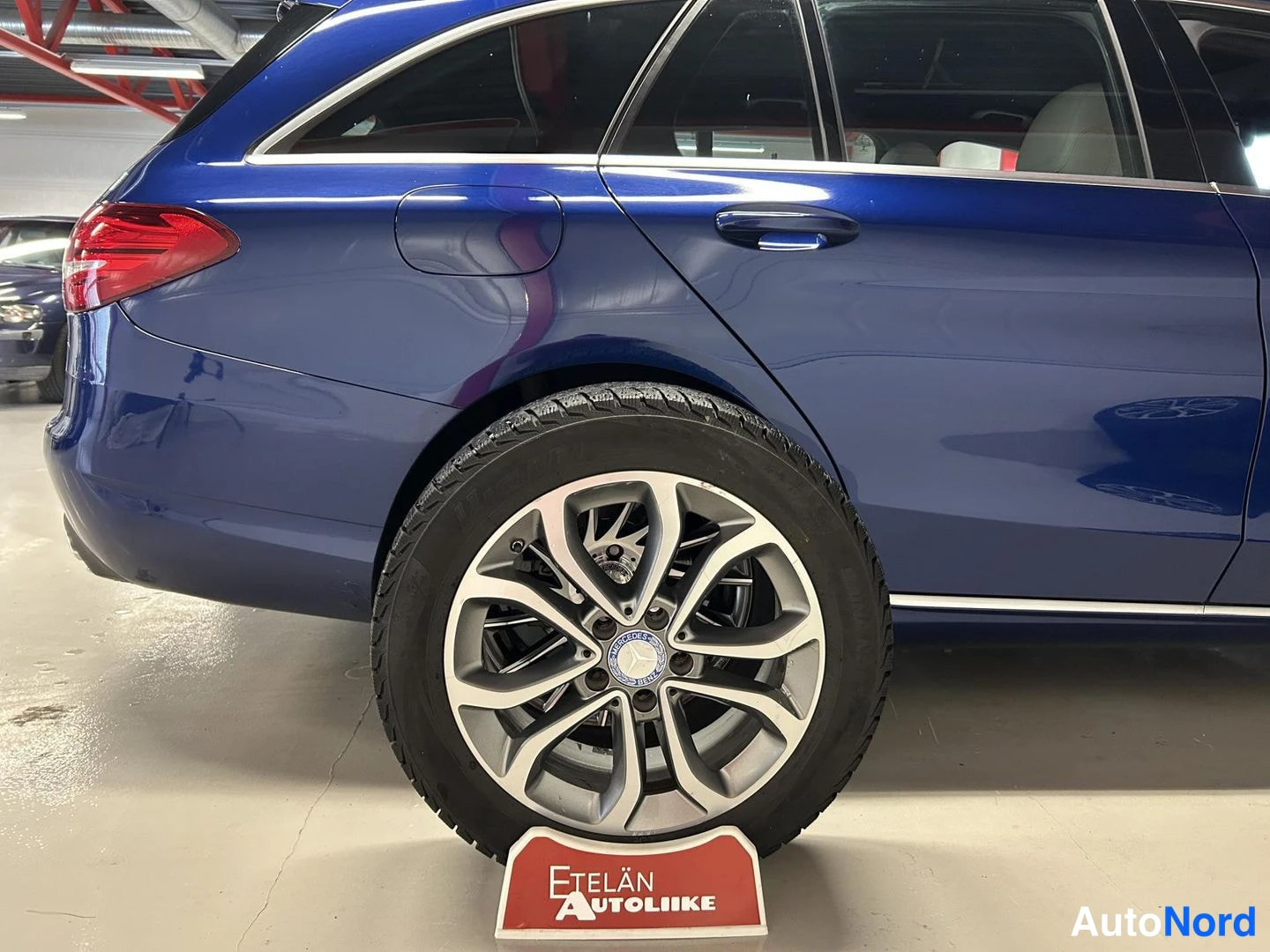 Takaviisto: Sinisen farmarikaupungin takapään ja takapyörän lähikuva, Mercedes-Benz-merkki pyörän navassa; auton alla punainen 'Etelän Autoliike' -kilpi.