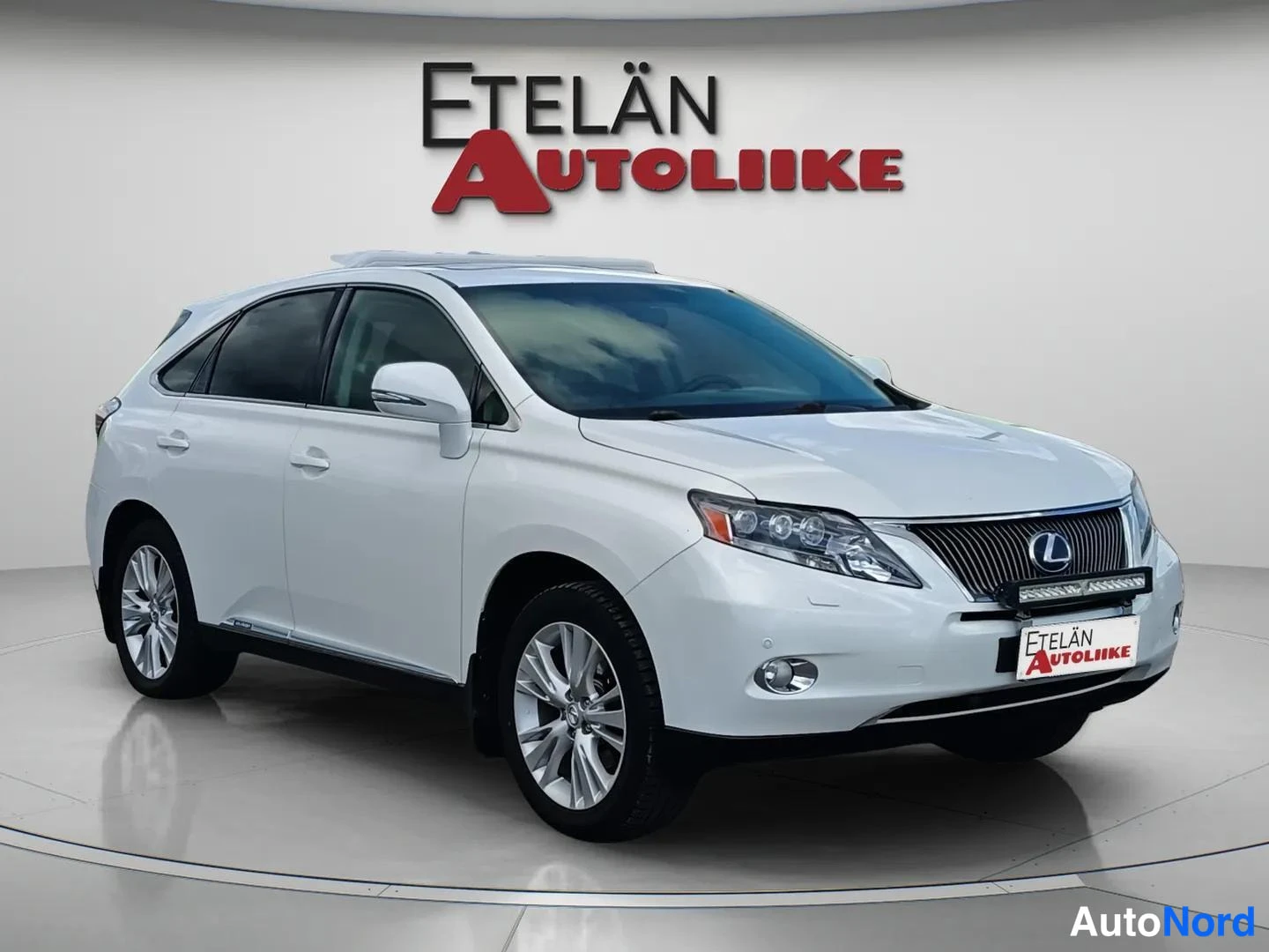 Etuviisto, nokka oikealle: Valkoinen Lexus RX farmarivalaisin kuvattu kolmeneljäsosakulmasta edestä oikealta; Etelän Autoliike -logo taustalla.