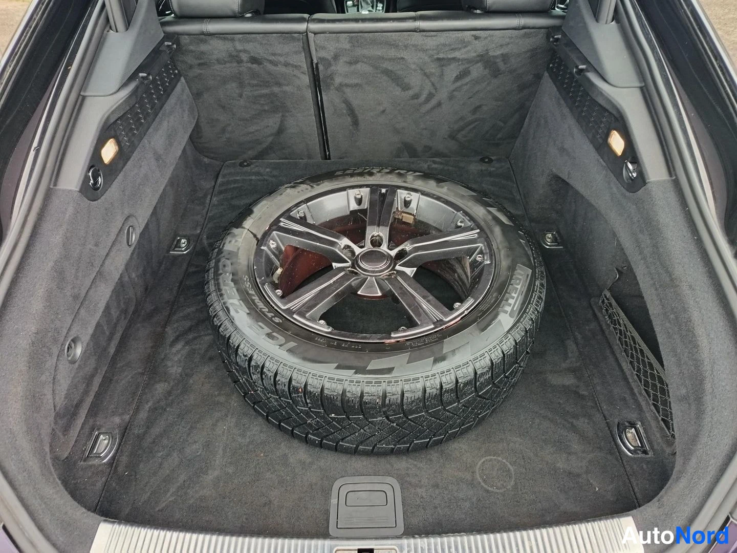Muu: Avoimet autotilan kuvat: auton tavaratila, jonka pohjalla on varapyörä Bridgestone Ice Cruiser -talvirenkaalla.