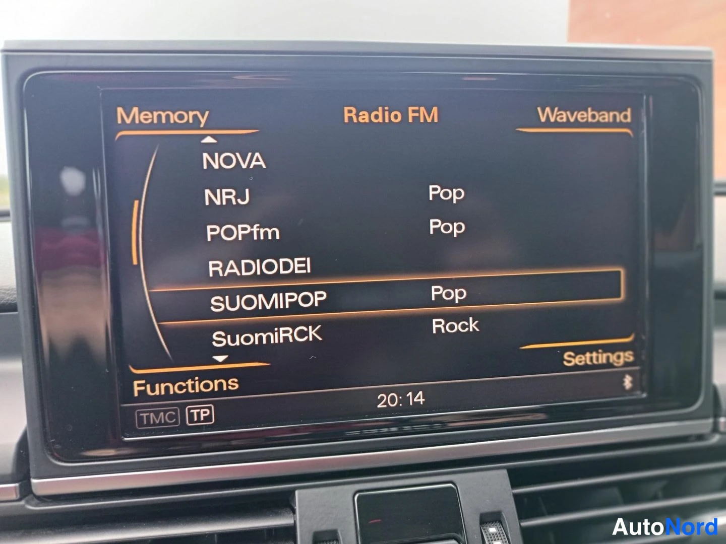 Muu: Auton infotainment-näyttö, jossa Radio FM -valikko listaa kanavat NOVA, NRJ, POPfm, RADIODEI, SUOMIPOP ja SuomiRCK kello 20:14.
