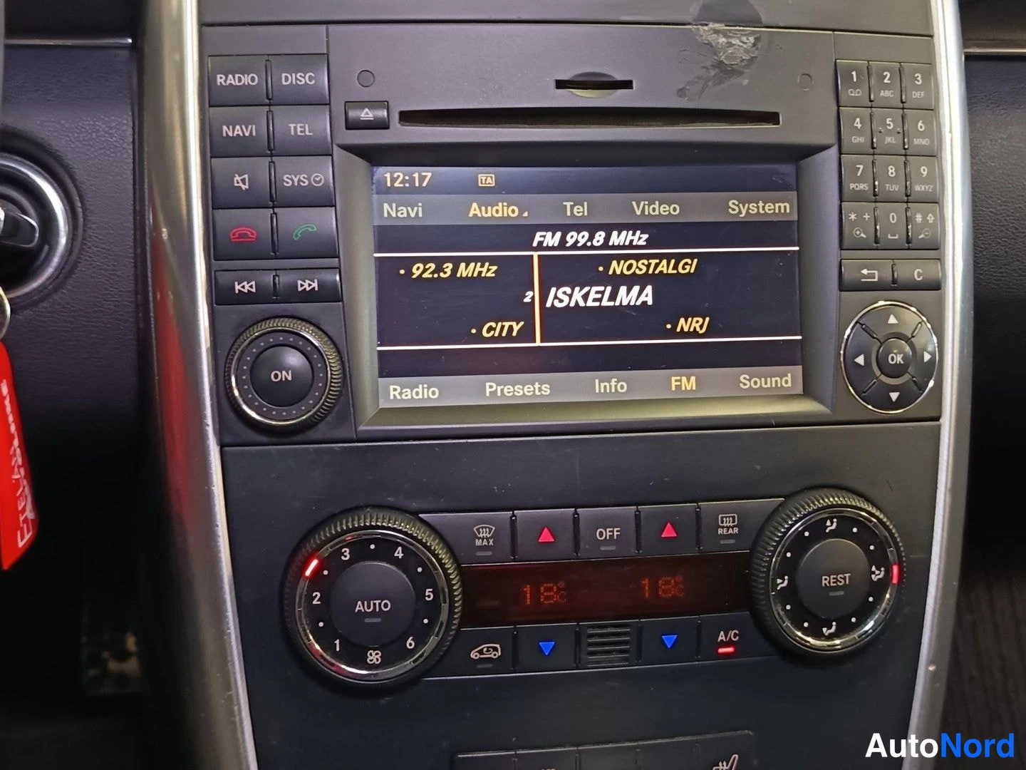 Muu: Keskikonsolin radio-navigointiyksikkö, näytöllä FM 99.8 MHz ja asemat kuten ISKELMA ja NOSTALGI. Alla automatiikkailmastoinnin säätimet, lämpötilat 18 °C ja A/C