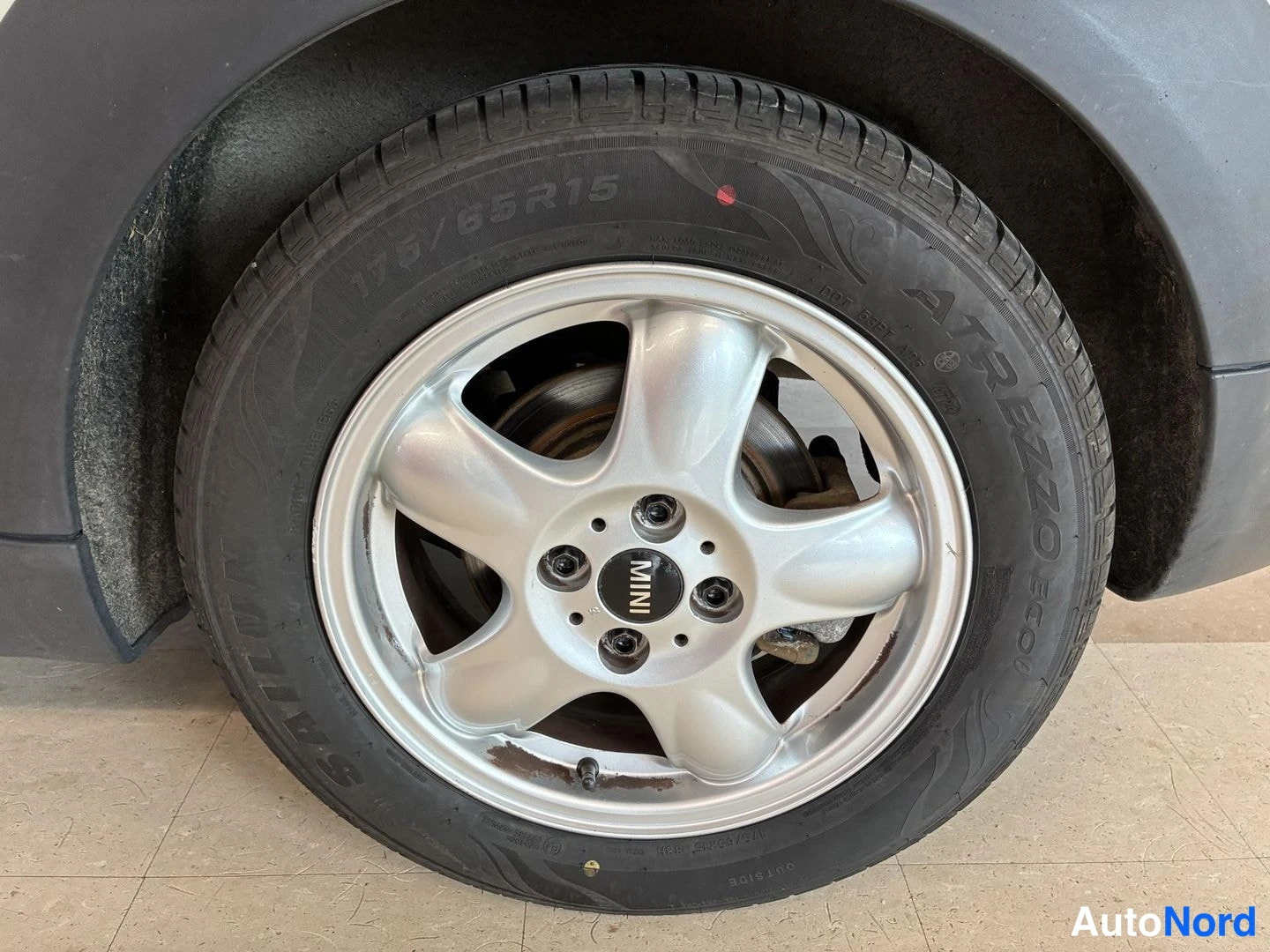 Muu: Auton rengas lähikuvassa, sivuseinämerkintä 175/65R15, hopeinen MINI-alkuvanne, jarrulevy takana näkyvissä.