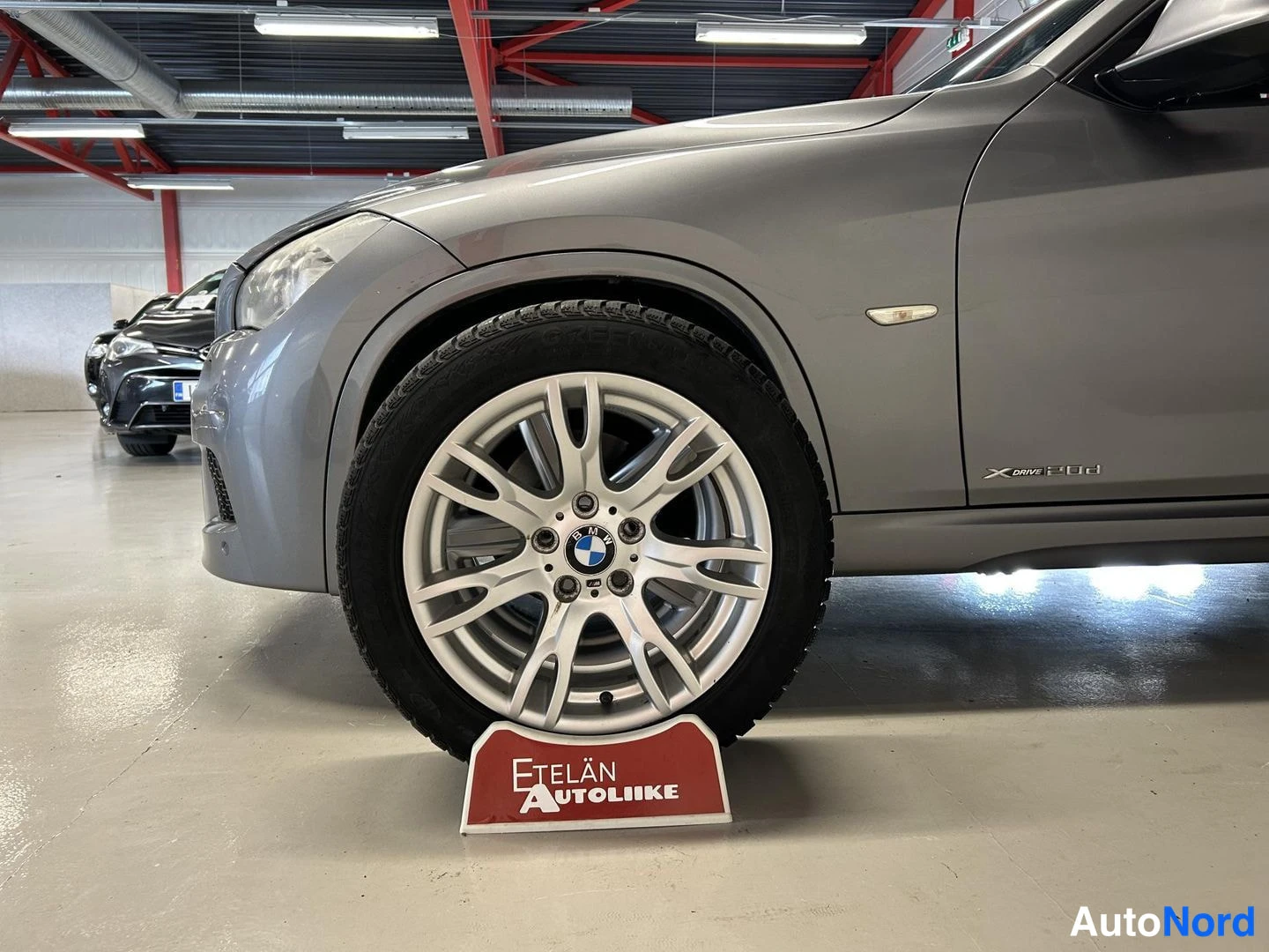Etuviisto, nokka vasemmalle: BMW:n etupyörä ja kevytmetallivanne, jossa BMW-logo, kori harmaa.