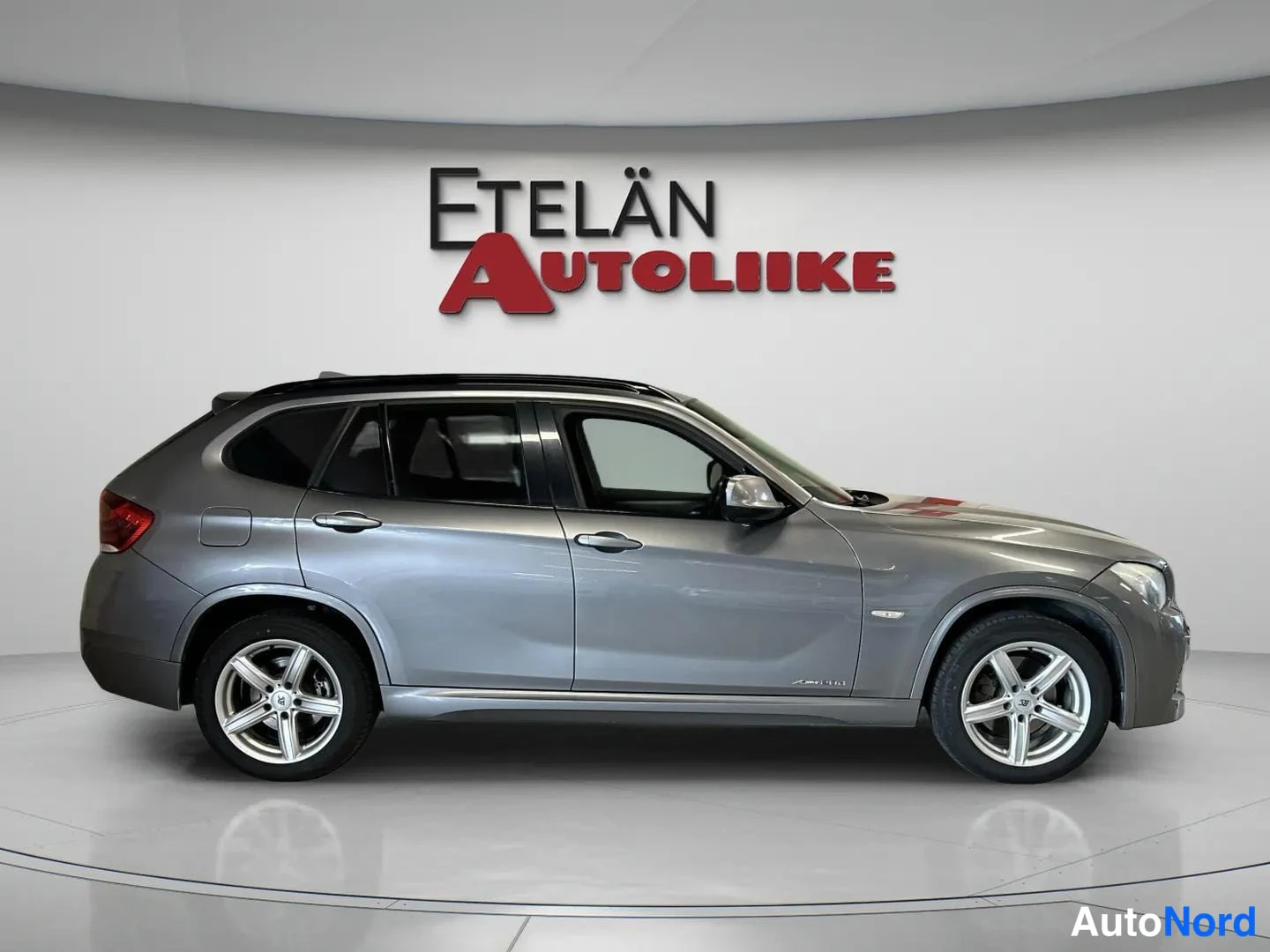 Etuviisto, nokka oikealle: BMW X1 sivulta viistosti edestä, kylki ja keulan etuosat näkyvissä, hopeanharmaa korimaali.