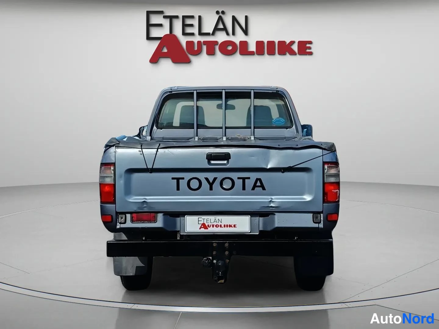 Takaa: Sinisen avolava-auton takanäkymä, Toyotan merkki lavan perässä ja vetokoukku alhaalla.