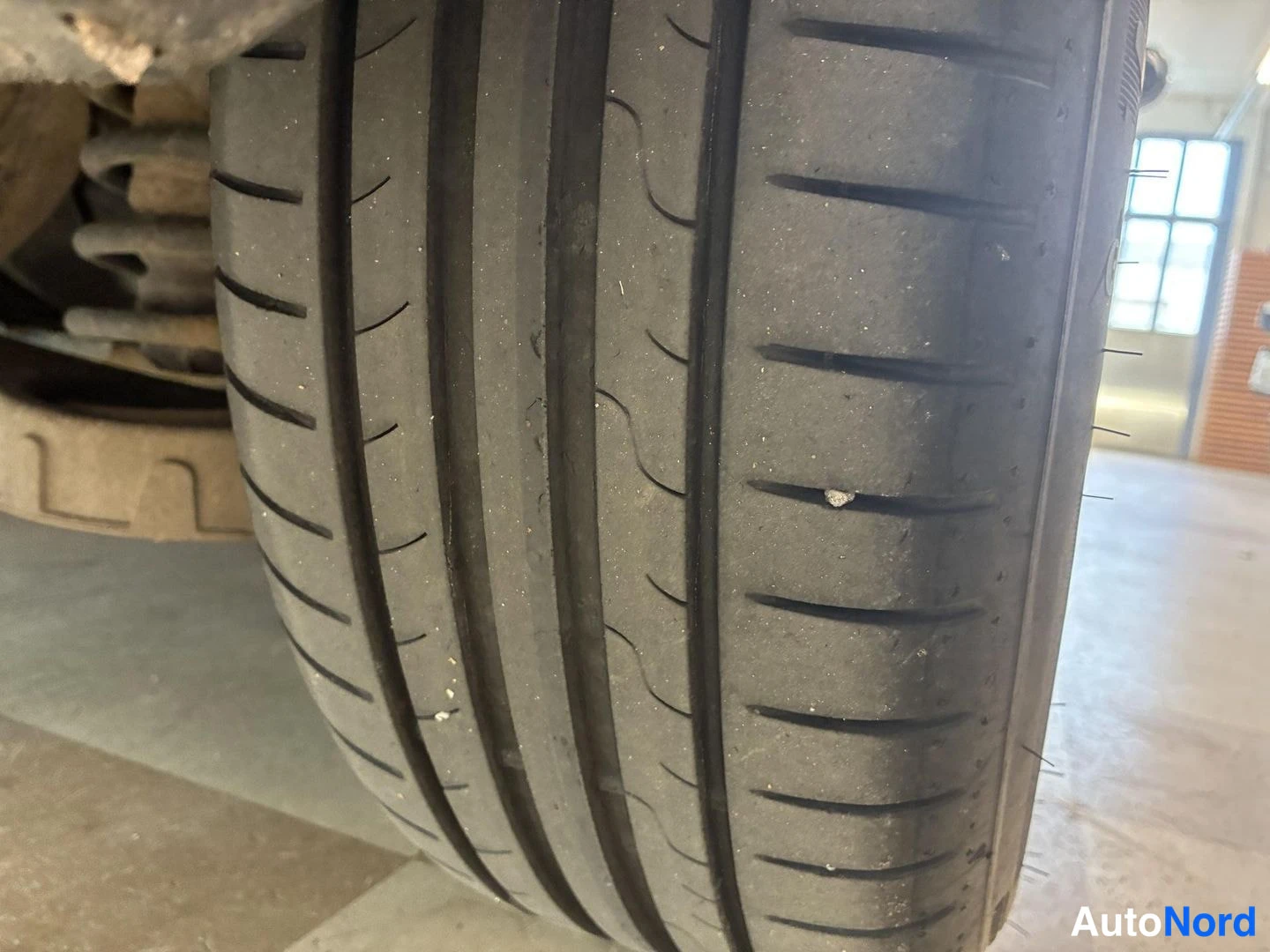 Yksityiskohta: Auton rengas lähikuvassa, kuvio ja pienet kevytmetalliosat erottuvat taustalla autotallin lattia ja ikkuna.