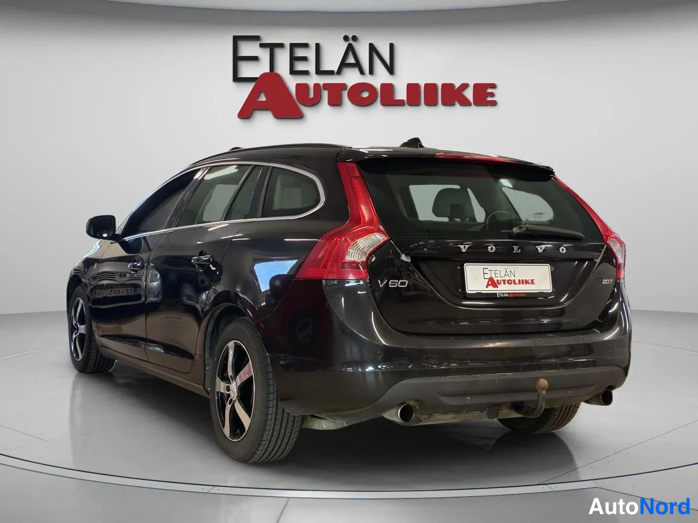 Takaviisto: Musta farmariauto takaa viistosti kuvattuna studio-olosuhteissa; takaluukussa VOLVO- ja V60-tekstit, perävaunukoulu ja kaksinkertainen pakoputki näkyvät.