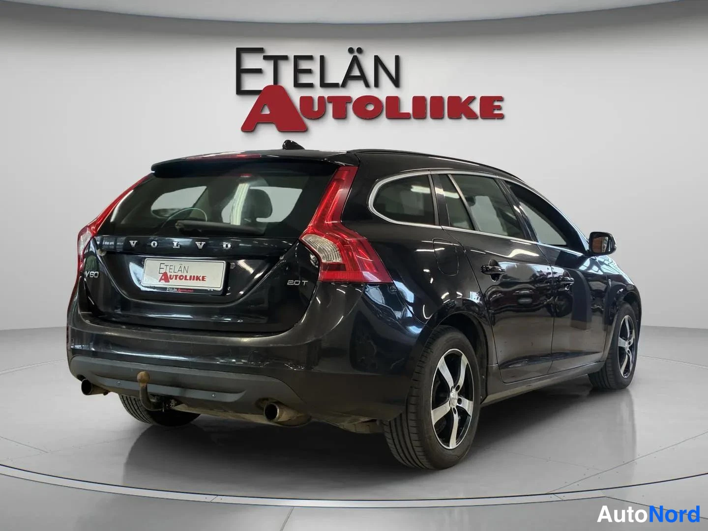 Takaviisto: Mustan farmariauton takanurkka ja oikea kylki kuvattuna; takaluukun VOLVO- ja 2.0T-tekstit, perävaunukoulu ja hopeavanteet näkyvät.