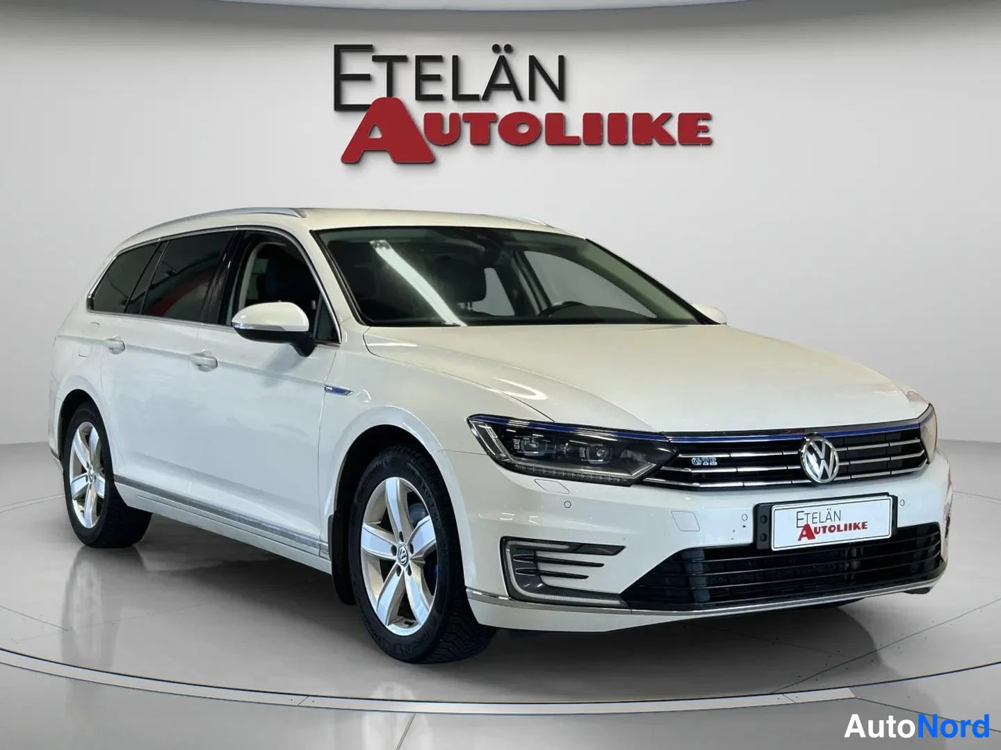 Etuviisto, nokka oikealle: Valkoinen Volkswagen Passat GTE -farmariauto kuvattu kolmannelta edestä oikealta, valokuvastudiovaalea tausta
