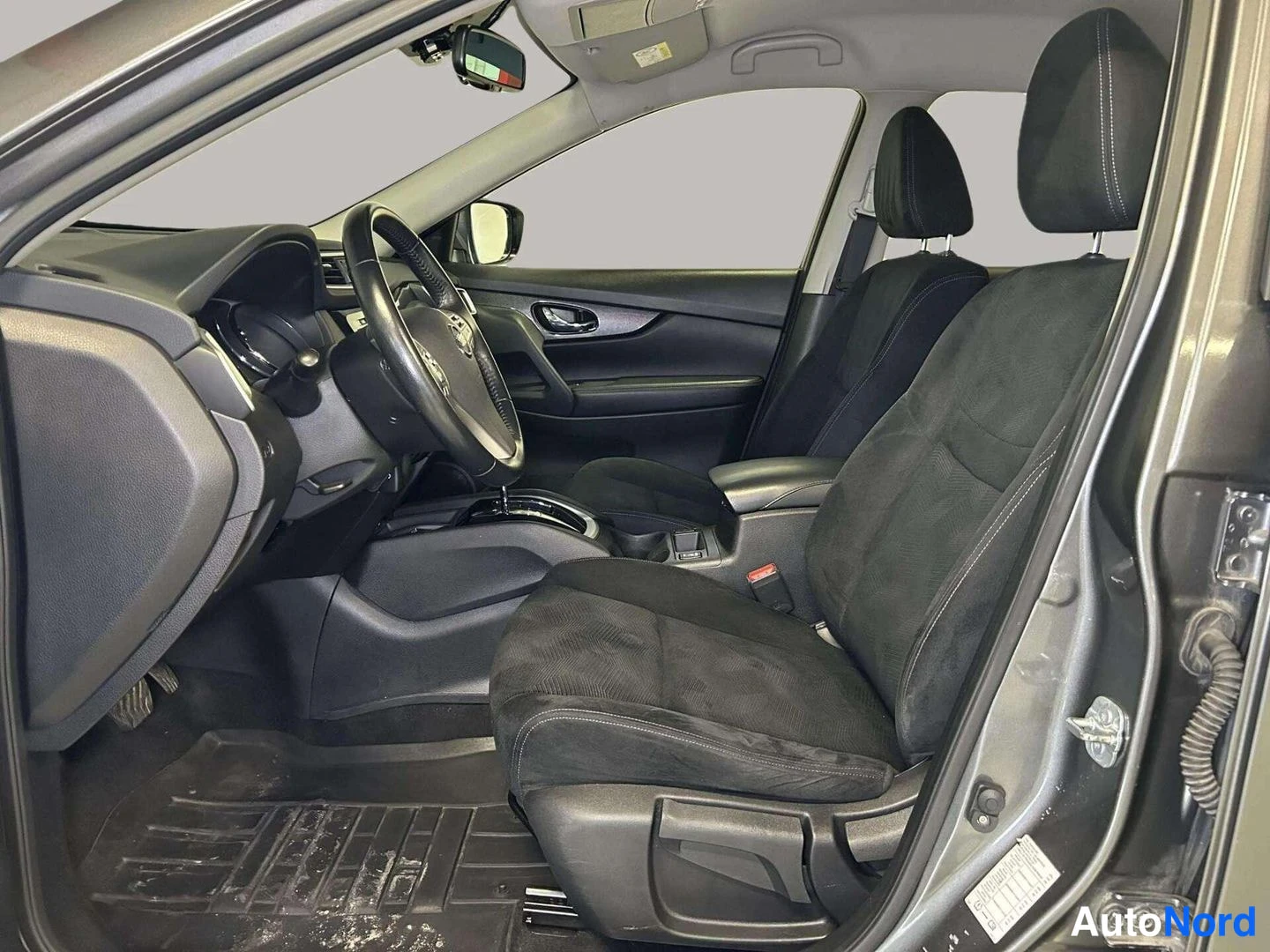 Muu: Nissanin sisätilat kuljettajan puolelta kuvattuna: musta ohjauspyörä, kangasistuimet ja keskikonsoli.