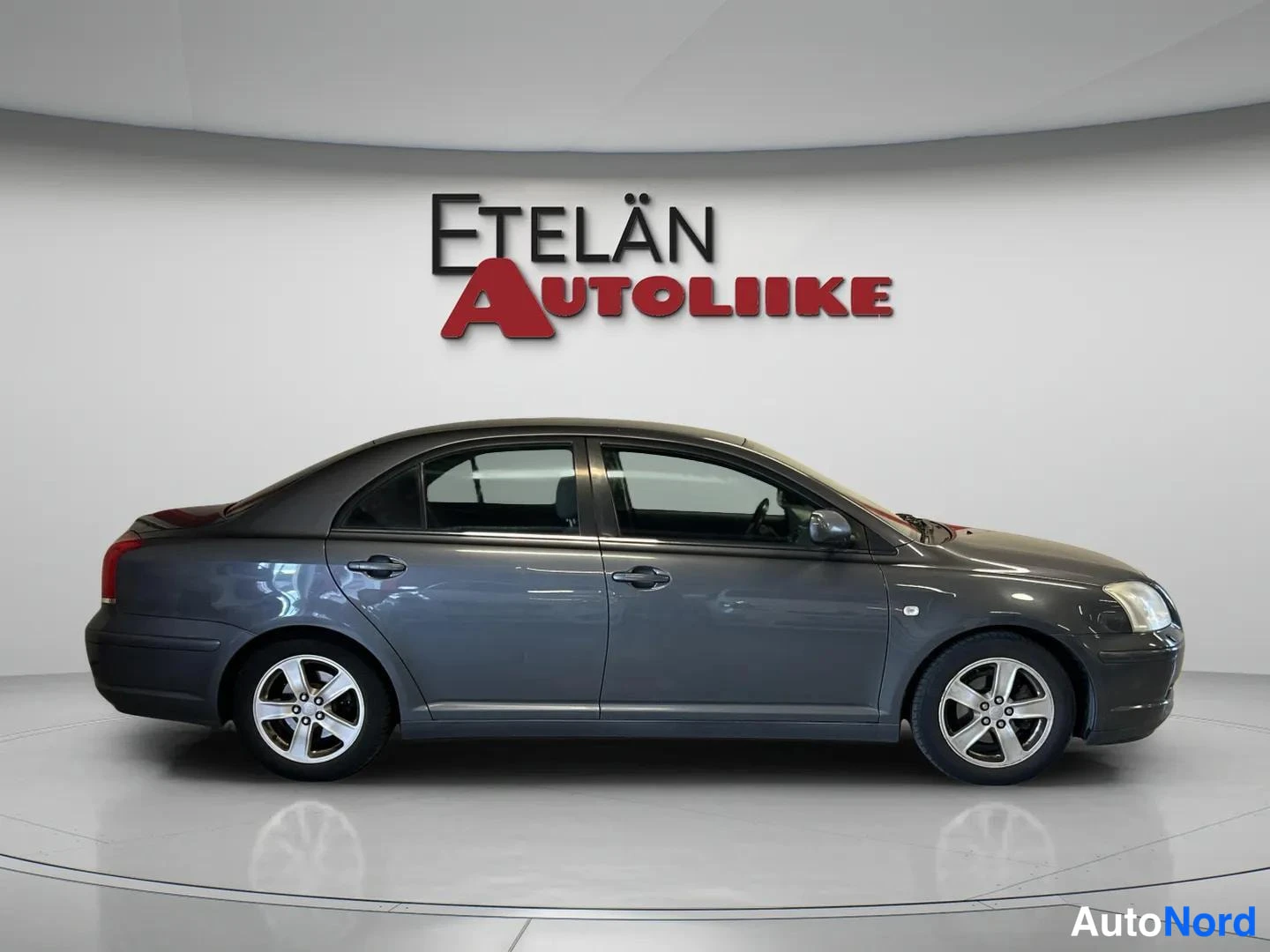 Sivulta: Toyota Avensis -sedan oikea kylki sivusuunnasta kuvattuna; viisiovainen tummanharmaa korstiili.