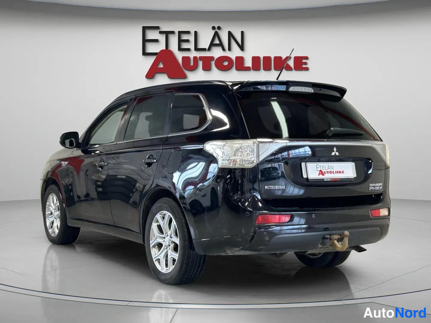 Takaviisto: Musta Mitsubishi Outlander kuvattu takaa-oikealta sivulta autoliikkeen showtilassa, takavaloissa ja takapuskurissa asennettu vetokoukku.
