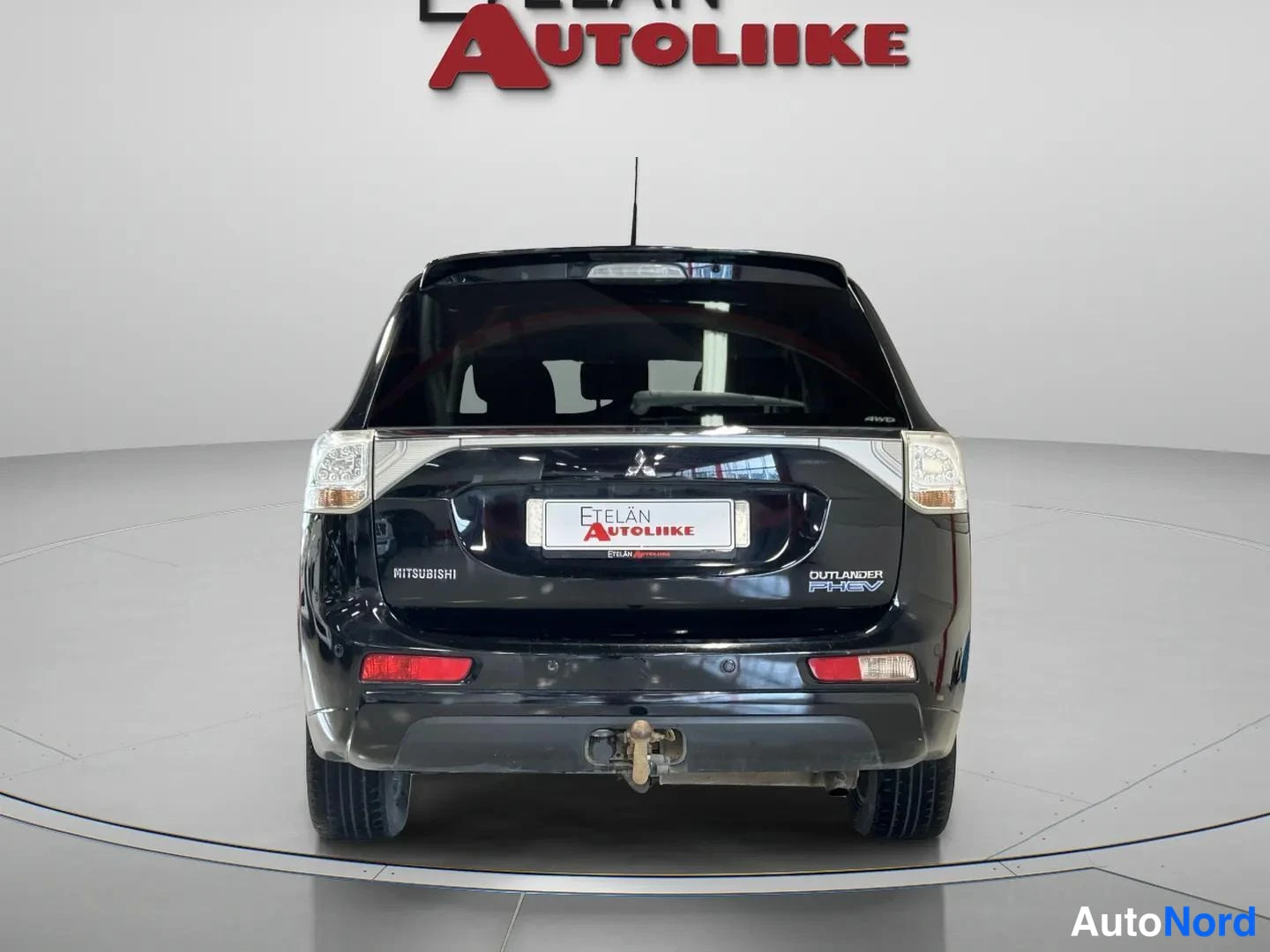 Takaa: Mustan Mitsubishi Outlanderin takanäkymä suoraan takaapäin; takaluukissa MITSUBISHI- ja OUTLANDER PHEV -tekstit, puskurissa vetokoukku.