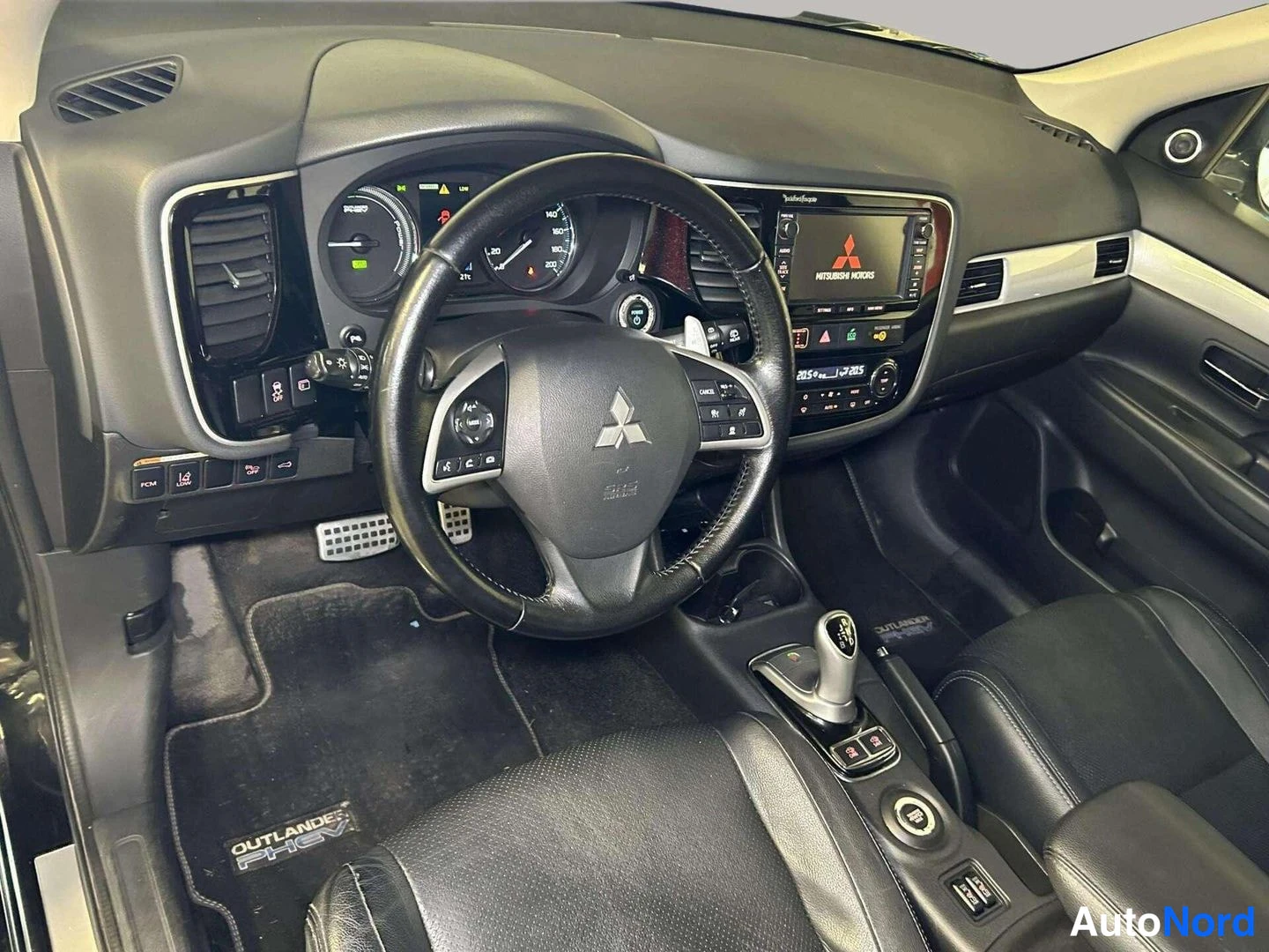 Muu: Auton sisätilat: vasemmalta ohjattu Mitsubishi-mustakalahdisella mittaristolla ja multimedianäytöllä, Outlander PHEV-mattoinen ovipellari ja kangaskäännityypin