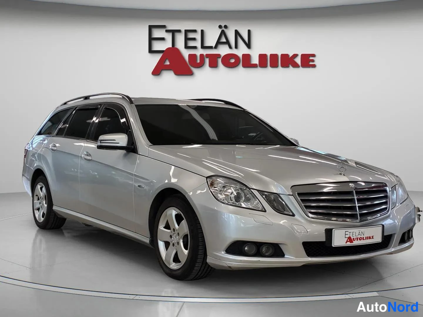 Etuviisto, nokka oikealle: Auton etukulmanäkymä: hopeinen Mercedes-Benz farmariauto studiossa, kylki ja etupää näkyvissä.