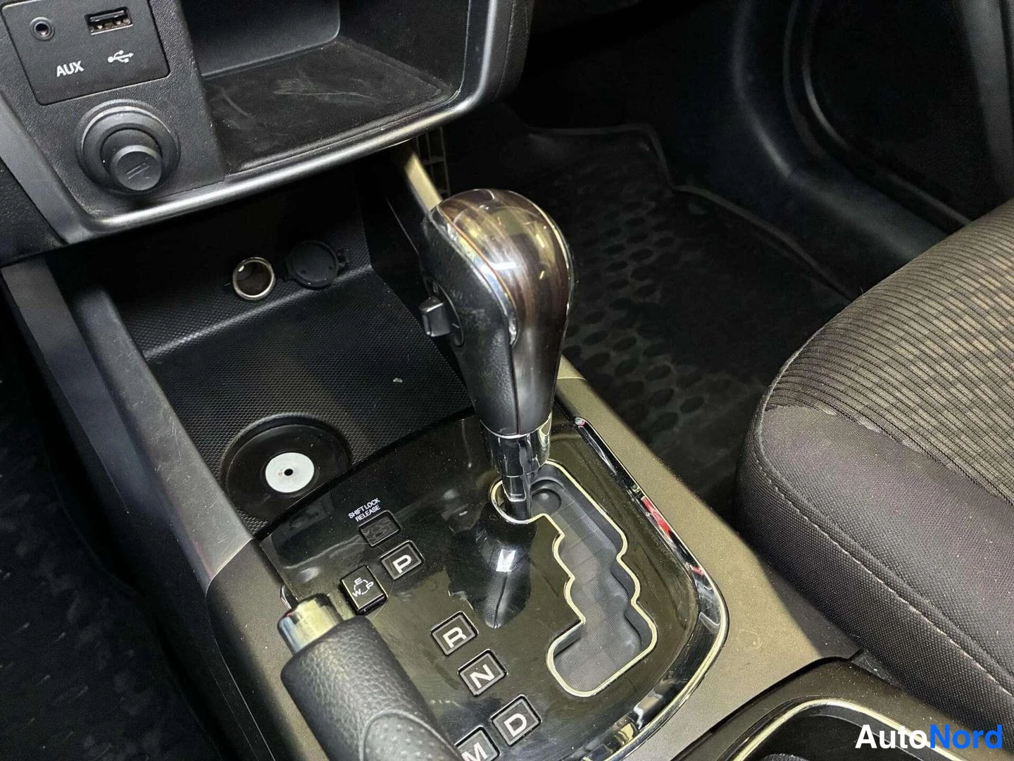 Muu: Automaattivaihteen valitsin korttelissa, napit P, R, N, D ja M näkyvät; myös käsijarru ja AUX/USB-liitännät.