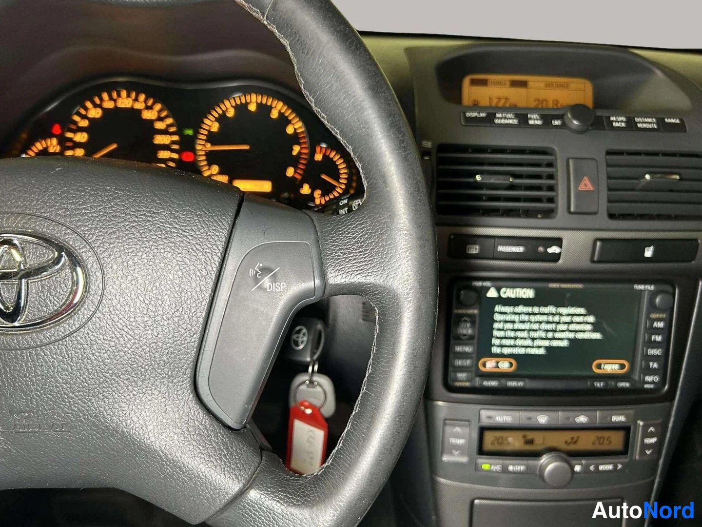 Muu: Kojelaudan ja keskinäytön lähikuva: Toyota-ratti DISP-painikkeella, näytössä CAUTION-varoitus englanniksi, alla automaattinen ilmastointipaneeli lukemin 28.5 ja