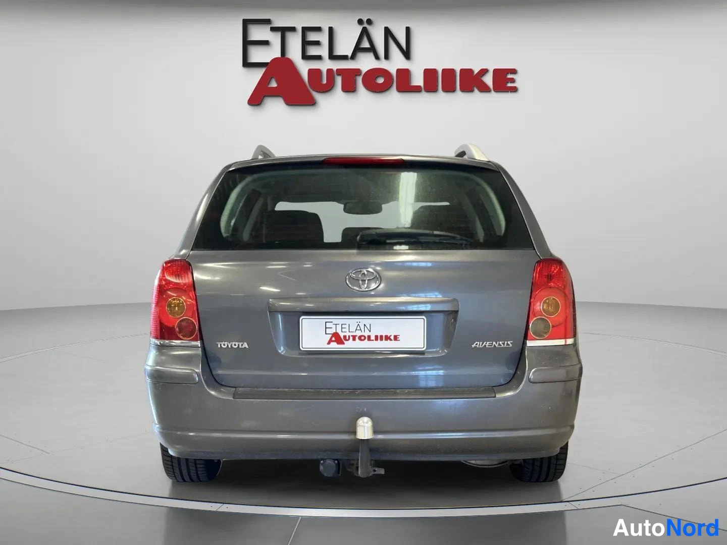 Takaa: Harmaan farmariauton takaosan suora kuva, takavalot ja TOYOTA- ja AVENSIS-tekstit näkyvissä.