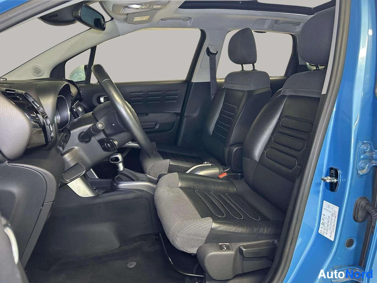 Muu: Auton sisätilat takaa oikealta kuvattuna: kaksi etuistuinta, ohjauspyörä ja automaattivaihteen valitsin; katossa panoramakaton reuna
