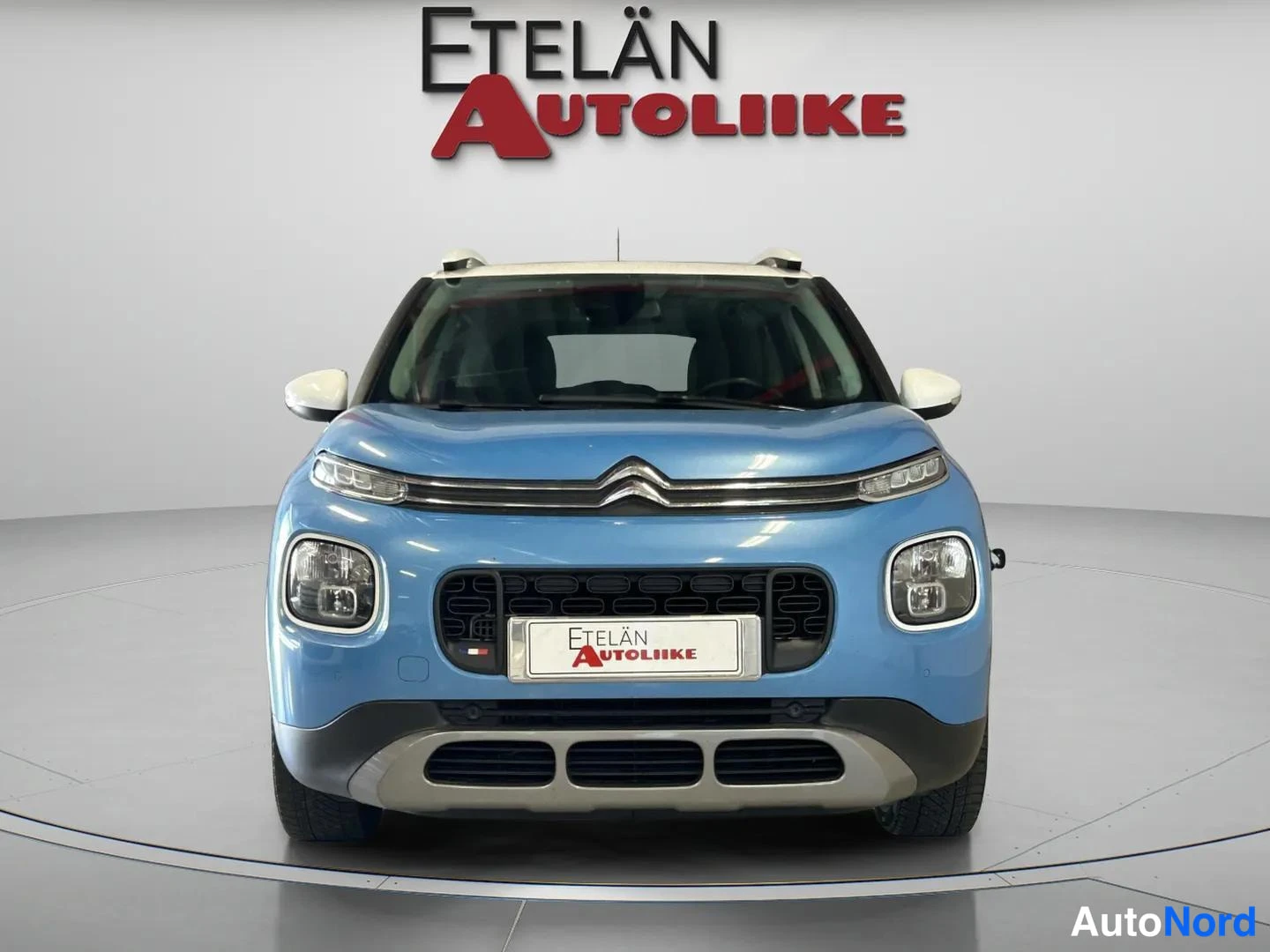 Edestä: Sinisen henkilöautin keula suoraan edestä: etuvazot, jäähynopero ja Citroën-merkki studion pyörivätä.
