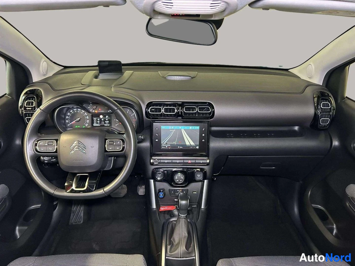 Edestä: Auton ohjaamo edestä: Citroen-ohjauspyörä, mittarit, keskellä kosketusnäyttö ja automaattivaihteen keila.