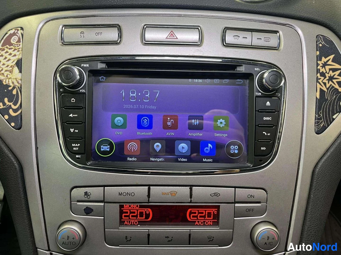 Edestä: Autoradion kosketusnäyttö, jossa DVD-, Bluetooth- ja navigointivalikot, alla ilmastointipaneeli.