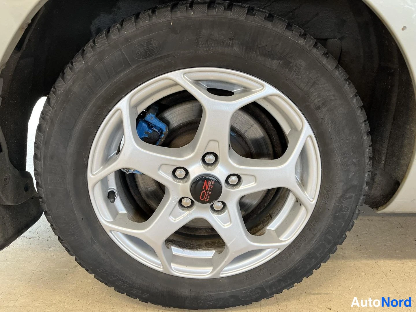 Muu: Lähikuva auton pyörästä: hopea viisipulttinen kevytmetallivanne ja nastarengas, jonka sivuseinässä Michelin-teksti.
