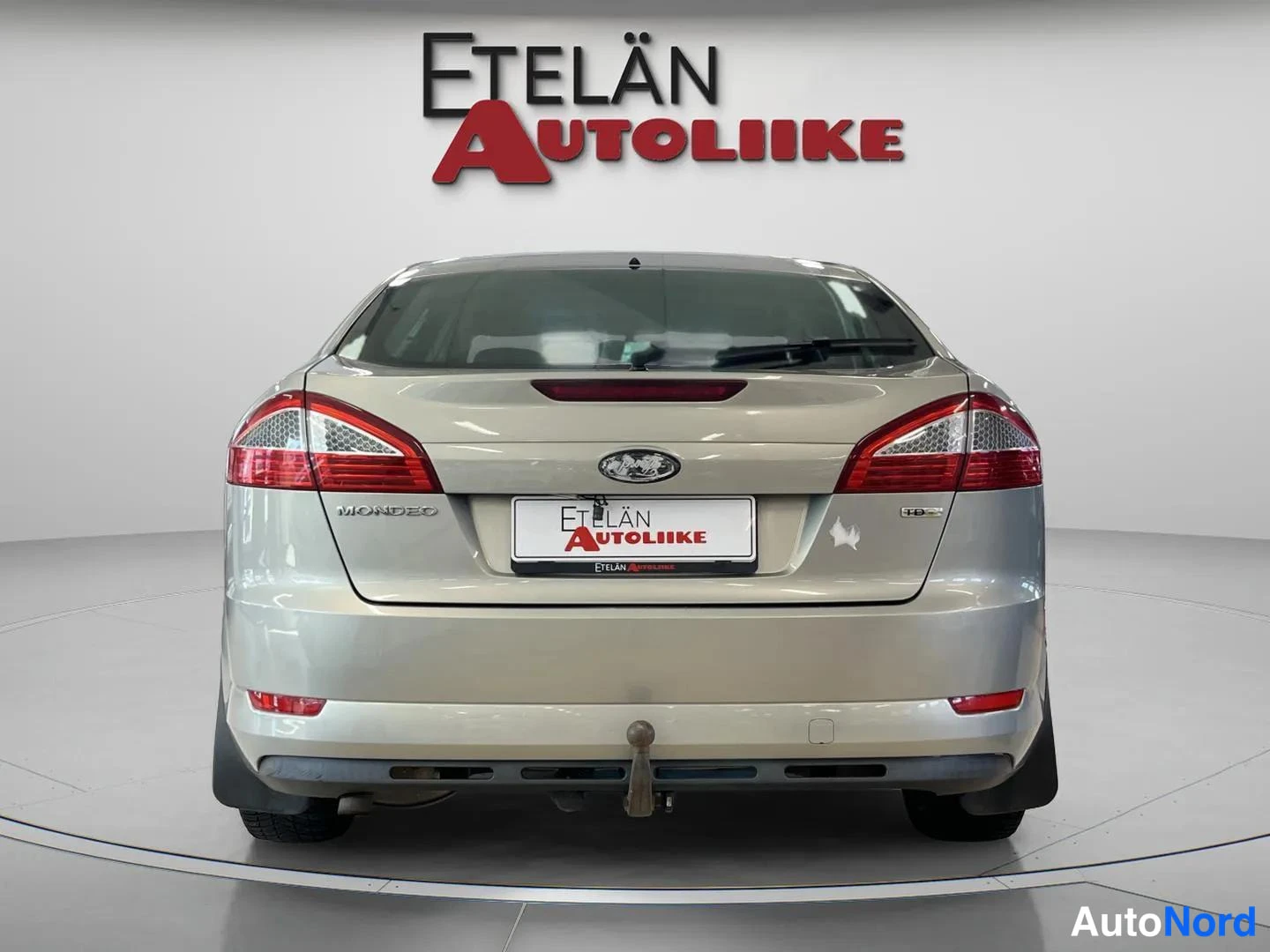Takaa: Auton takaosa suoraan takaa; beige Ford Mondeo, takavalojen, MONDEO-merkinnän ja Etelän Autoliike -rekisterikilven näkyvissä.