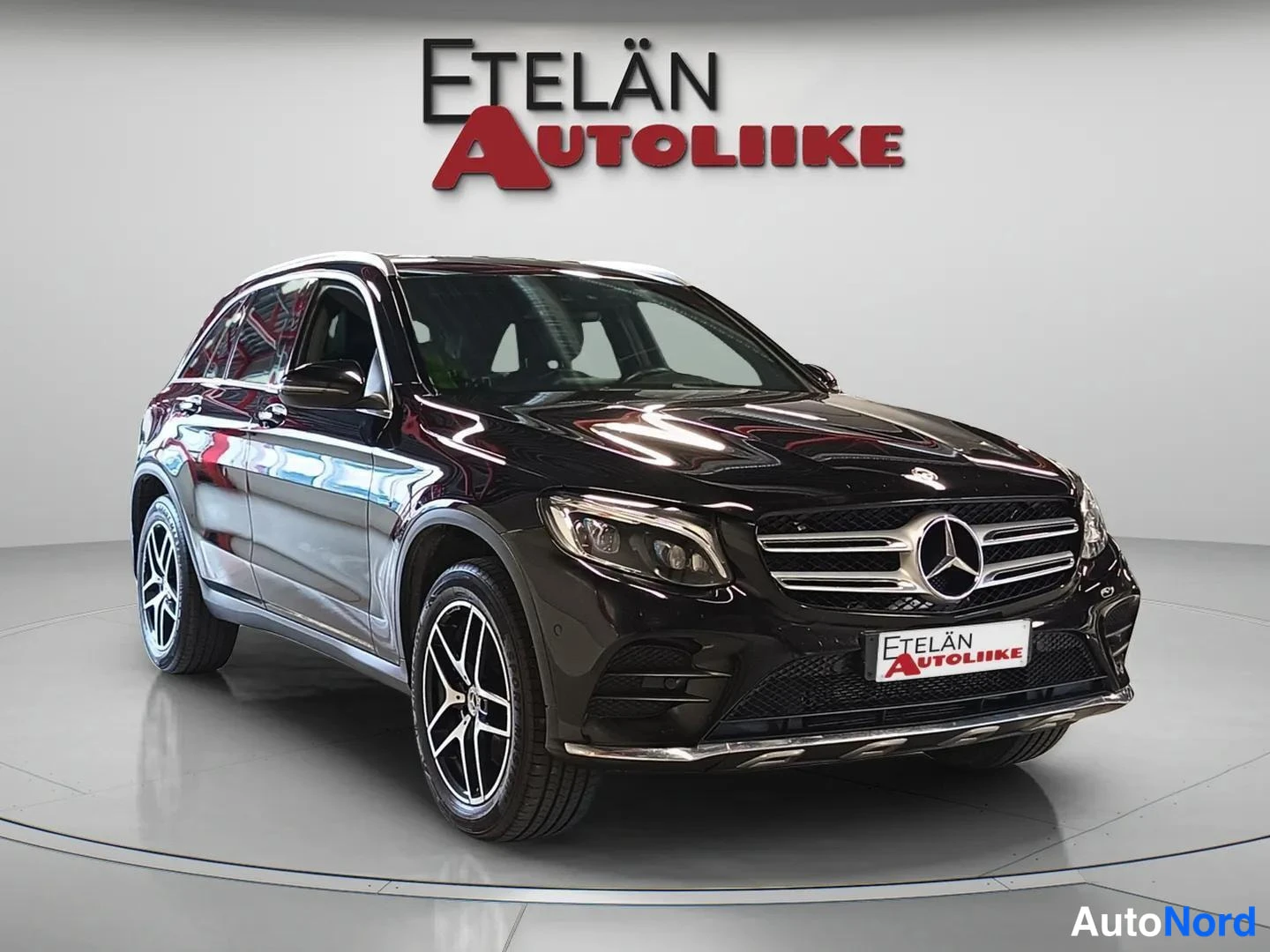 Etuviisto, nokka oikealle: Musta Mercedes-Benz GLC -maasturi etuviistosta valokuvastudiossa, Edelän Autoliike -logo taustalla ja etupuskurissa.