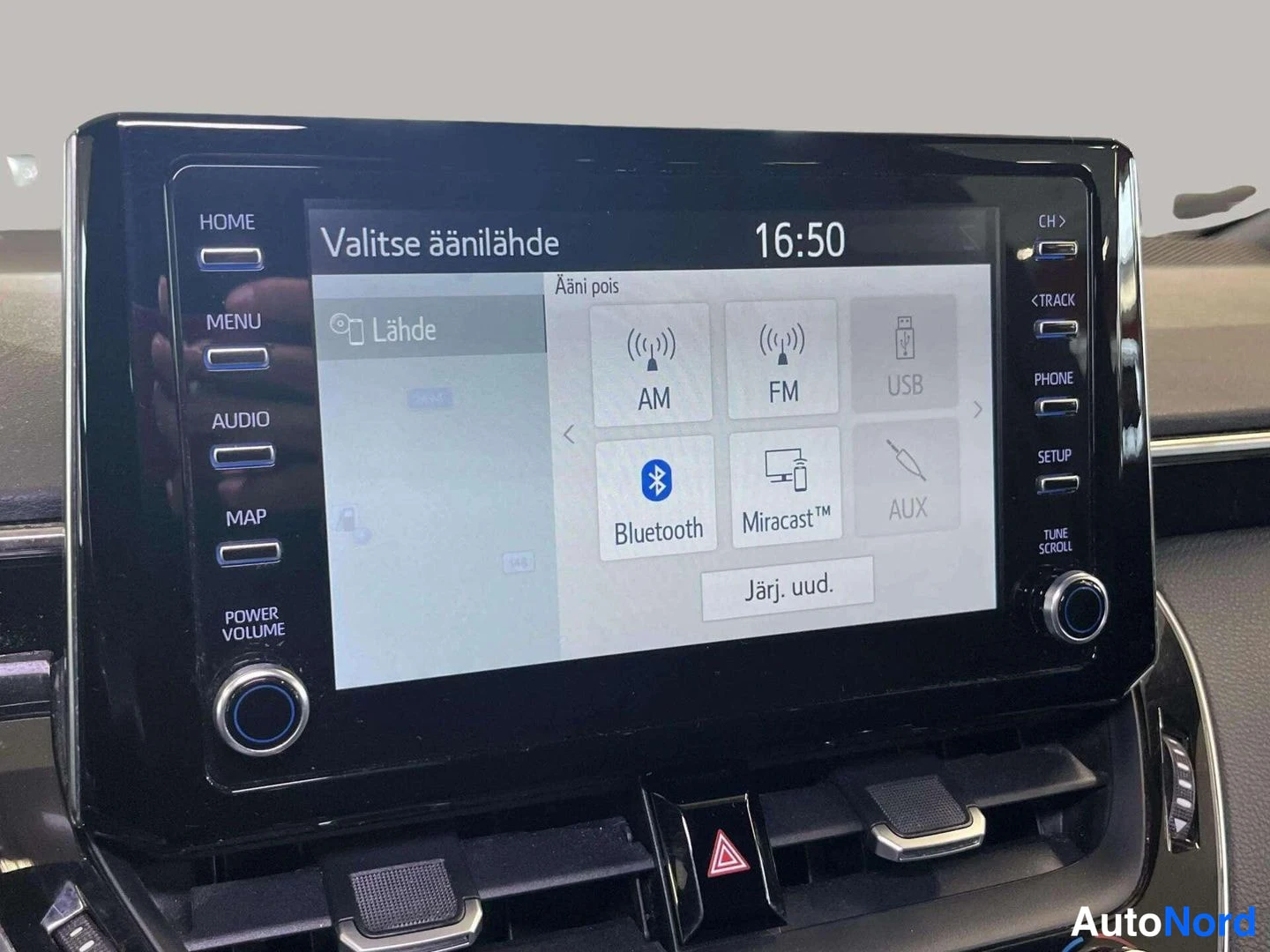 Muu: Ajoneuvon keskusnäyttö näkyy lähikuvassa; ruudulla teksti 'Valitse äänilähde' ja vaihtoehdot AM, FM, USB, Bluetooth, Miracast ja AUX; kellonaika 16:50.