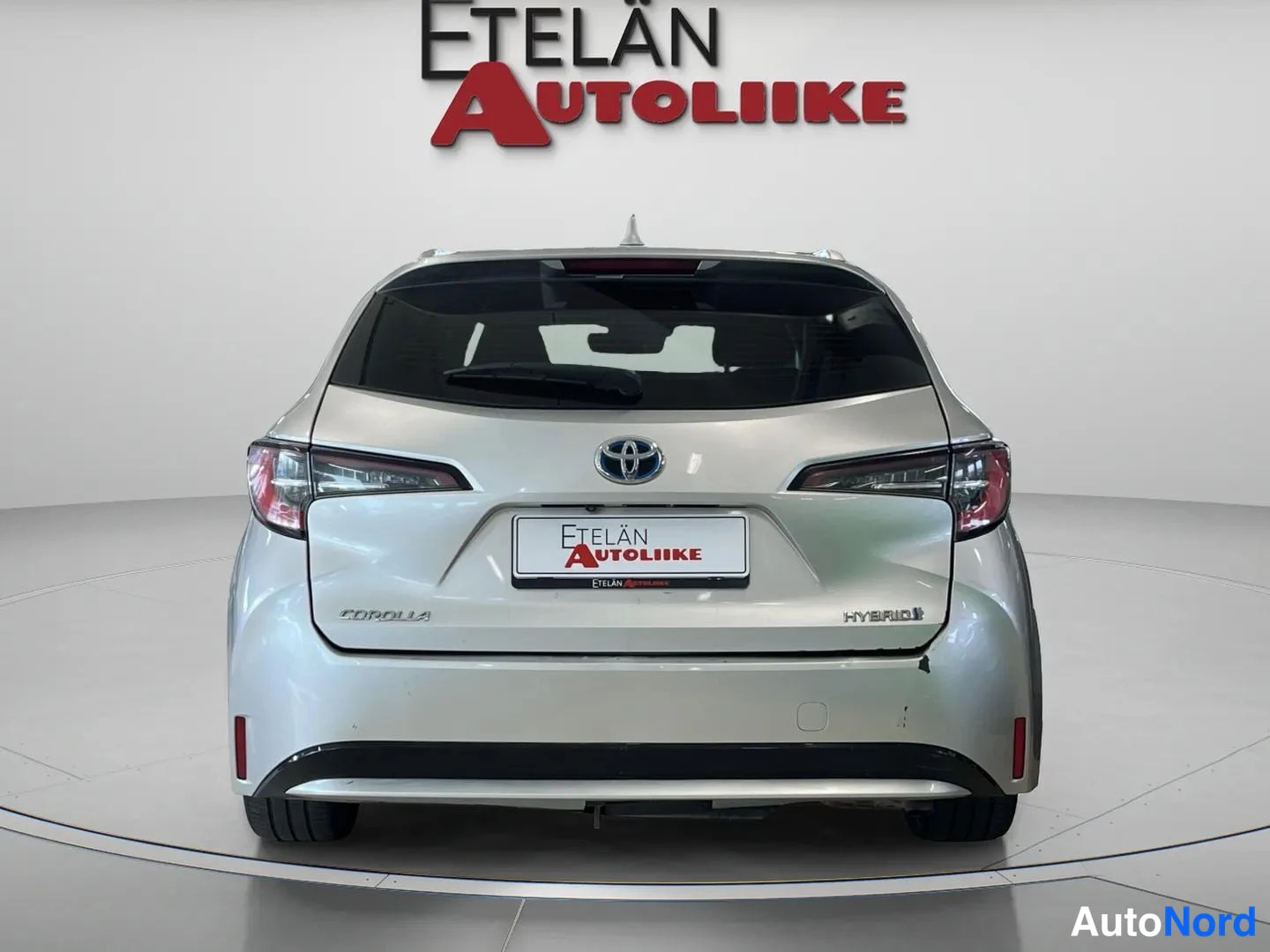Takaa: Hopeanvärinen Toyota Corolla -farmari suoraan takaa kuvattuna, takaluukussa HYBRID-merkintä.