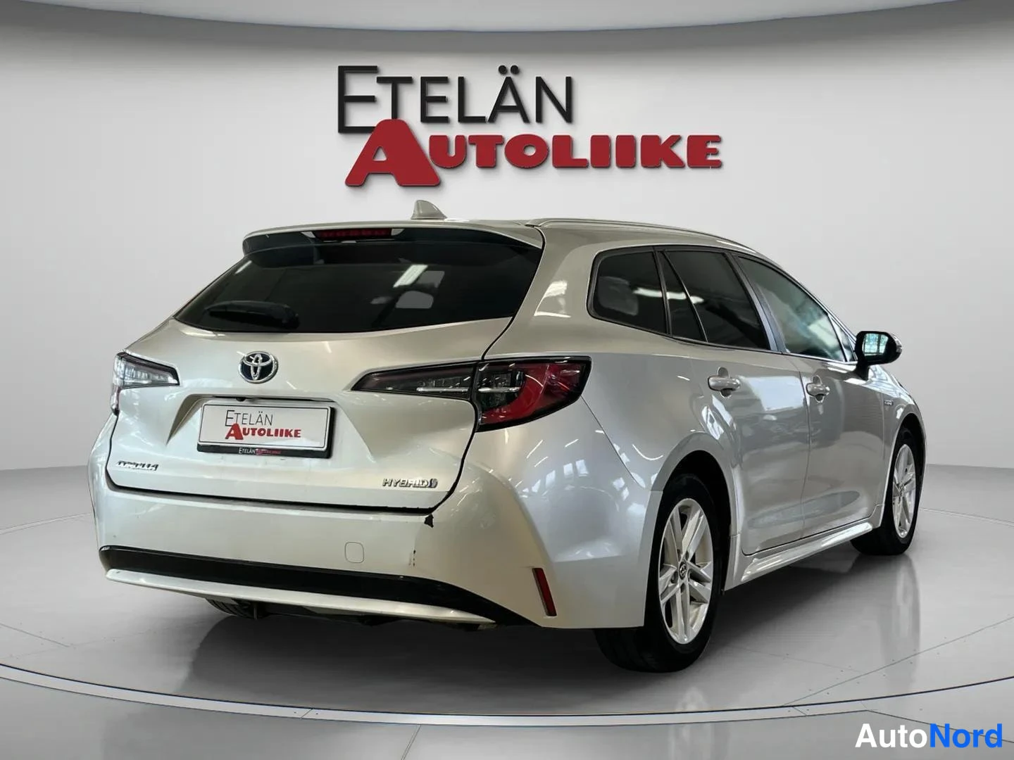 Takaviisto: Hopeanvärinen Toyota Corolla -farmari takaa toiselta sivulta kuvattuna, HYBRID-merkintä takaluukussa.