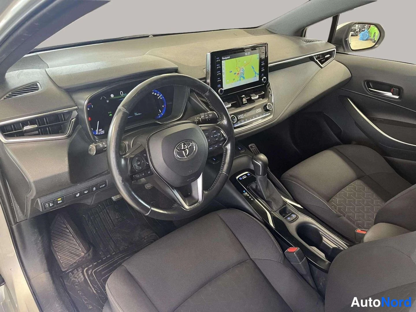 Muu: Auton etupenkin ja kojelaudan näkymä: Toyota-monitoimiohjauspyörä, hybridi-mittaristo, kartta kosketusnäytössä ja automaattivaihteen valitsin keskikonsolissa.
