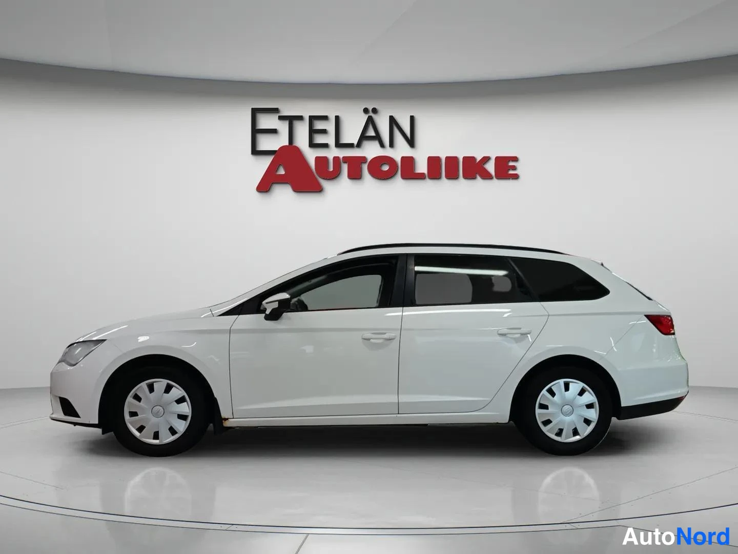 Sivulta: Side view of a white estate car showing doors and wheels in a dealership studio.