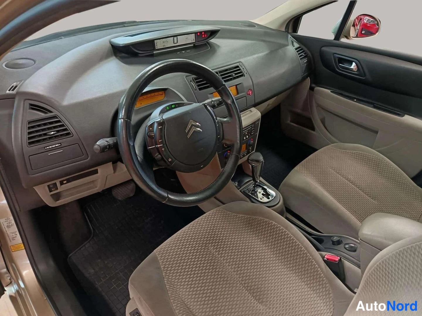 Muu: Citroënin kuljettajan puolen sisätila: ohjauspyörä, mittaristo ja tumma kojelauta, automaattivaihteen valitsin ja beige-tkankaat etuistuimet.