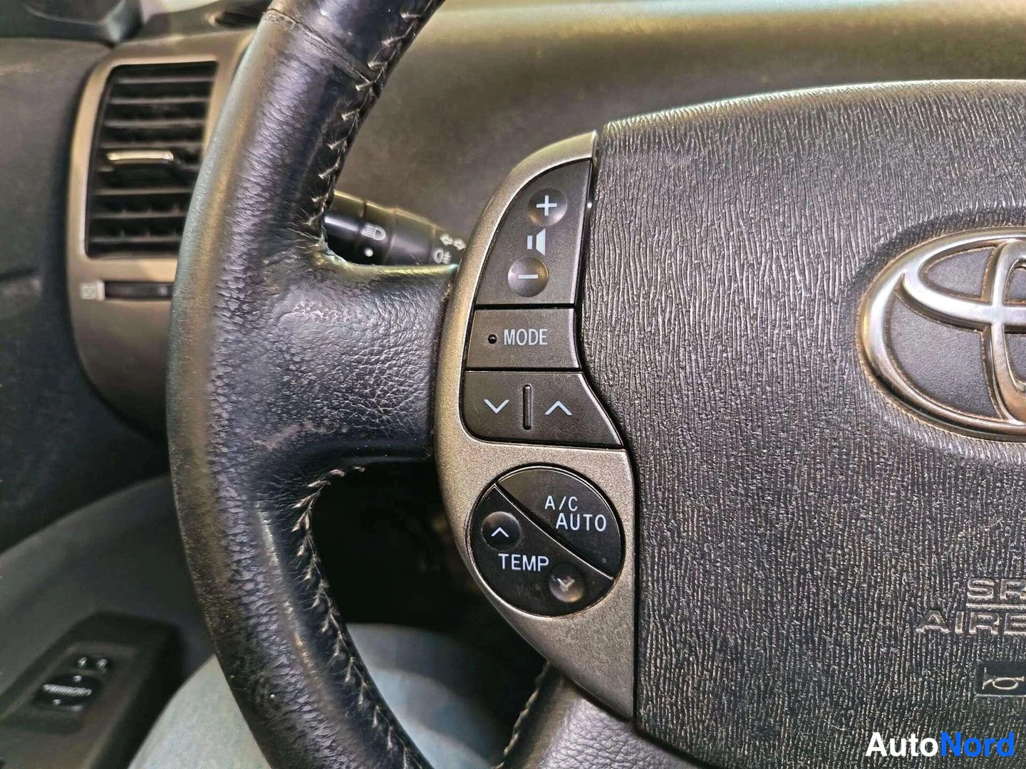 Muu: Ohjauspyörän sivupaneeli A/C AUTO- ja TEMP-painikkeilla sekä tilapainikkeilla MODE, +/- ja nuolilla; Toyota-emblem näkyy ohjauspyörän nappaa.