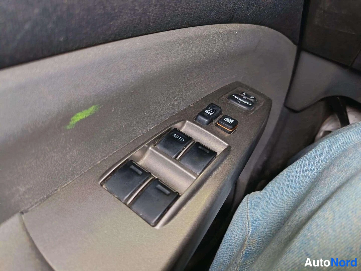 Muu: Auton oven sähköikkunan nappiryhmä: AUTO-merkittyä nappia, lukitus- ja peilinäppäimiä sekä kaksi muuta ikkunannostinnappia; kangaspinta ohjaajan reisellä.