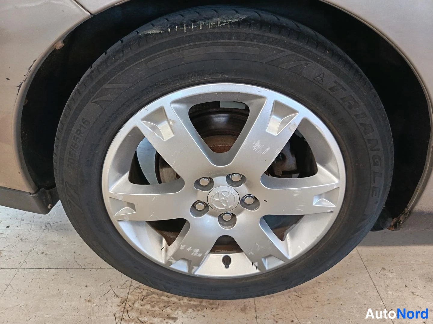 Yksityiskohta: Sivukulma auton pyörästä: hopeinen Toyota-alumiinivanne ja musta rengas, jonka sivussa lukee 195/55R16.