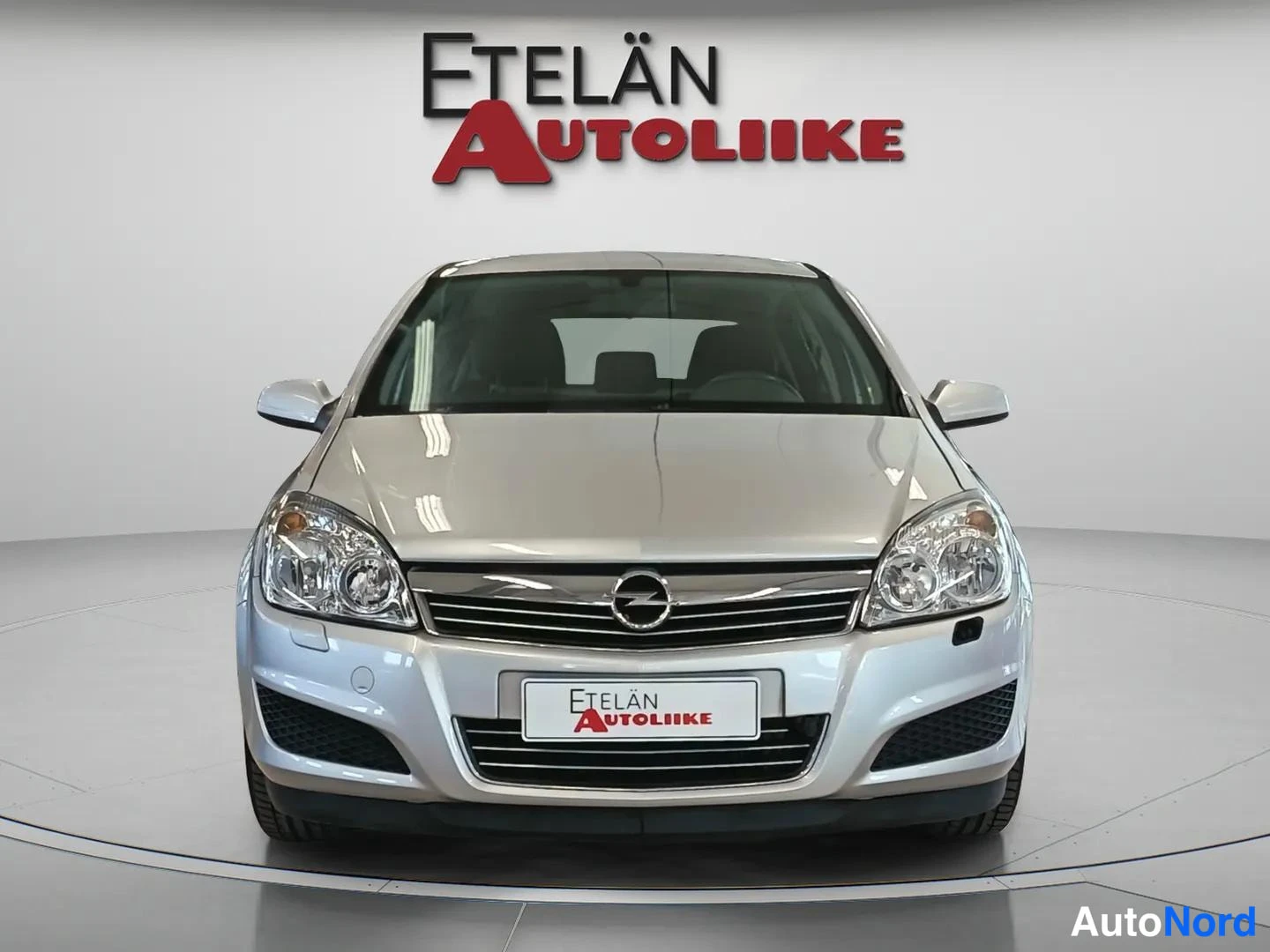 Edestä: Hopeanvärinen Opel Astra edestä päin studio-valkoinen tausta, Etelän Autoliike -logo ylhäällä.