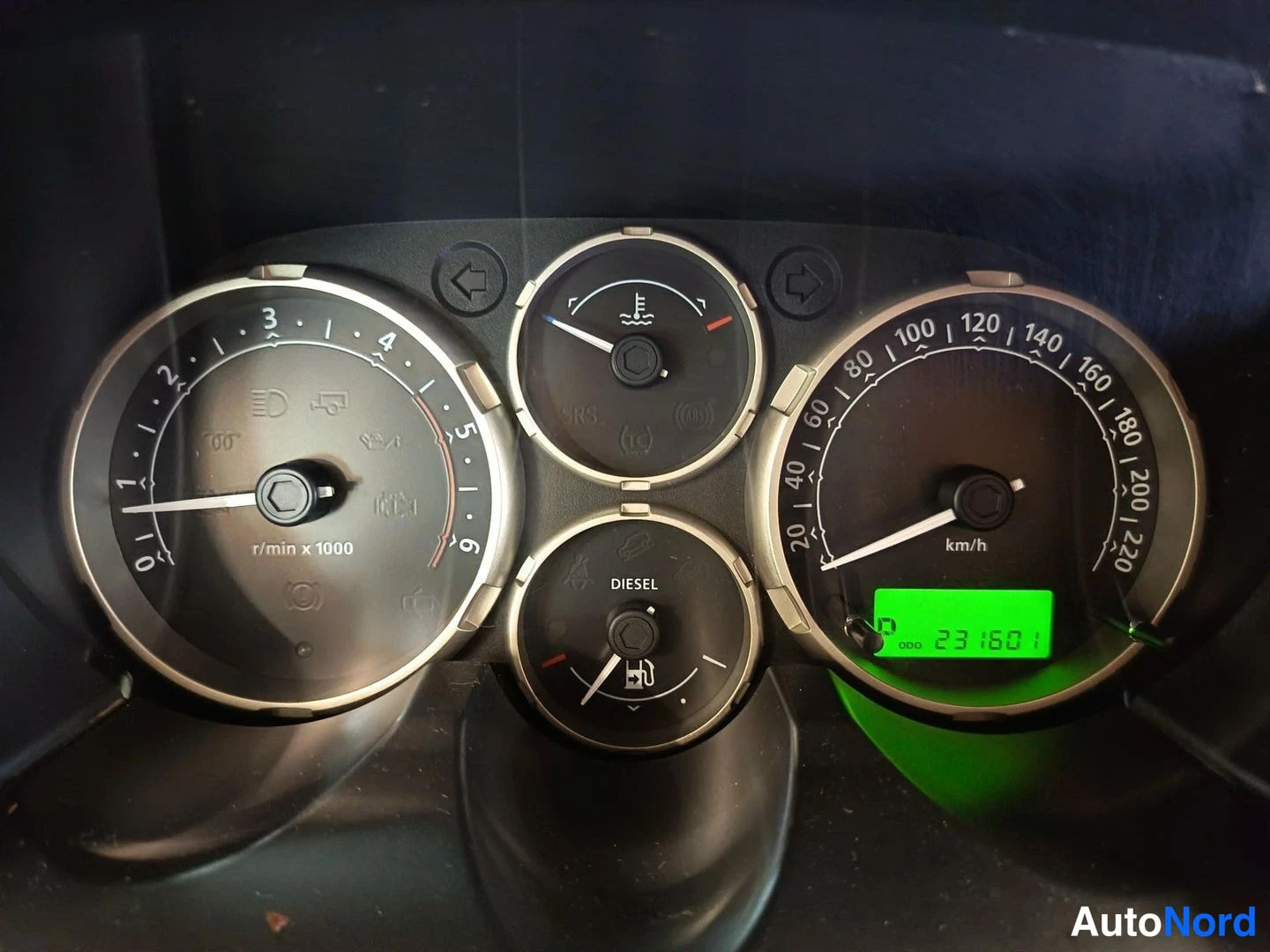 Yksityiskohta: Close-up of instrument cluster showing four gauges: rev counter on left, speedometer (km/h) on right reading 23160.8 km on green digital display, smaller centre